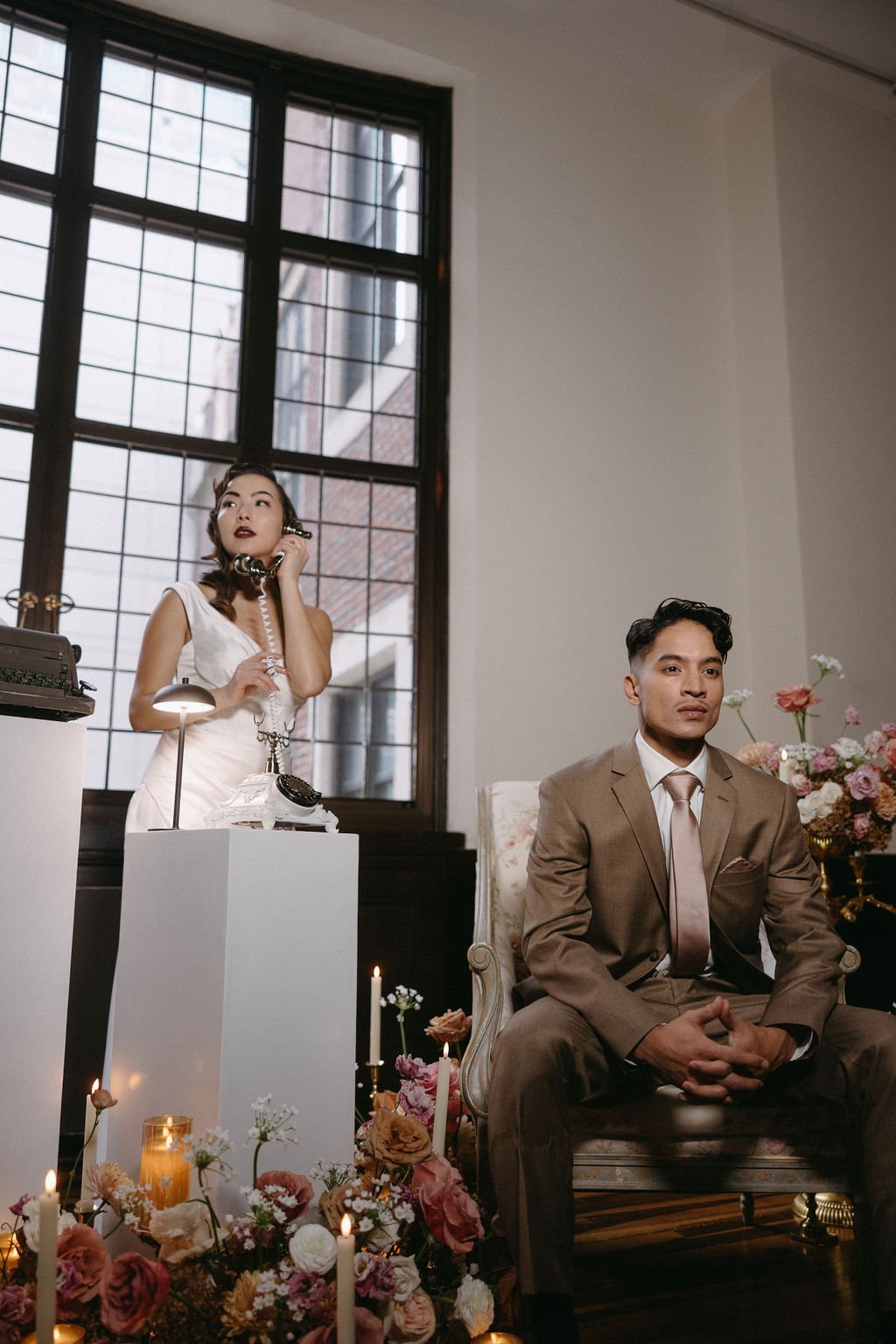 Bride and groom posing together in front of an industrial grid window with warm ambient room lighting.