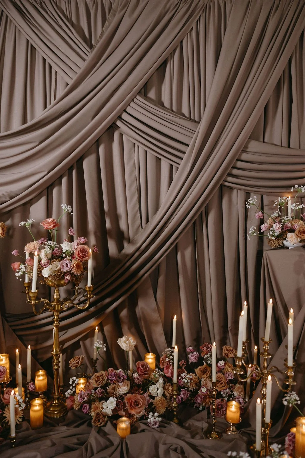 Textured beige fabric draping paired with warm-toned wedding floral arrangements and glowing candelabras for a vintage aesthetic.