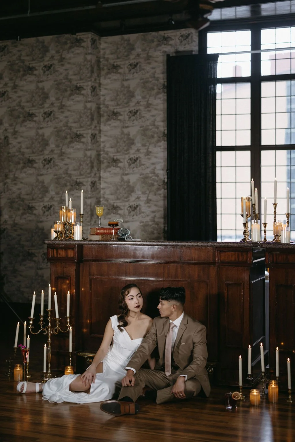 Couple posing by an antique dark wood bar framed by glowing taper candles and vintage architectural details.