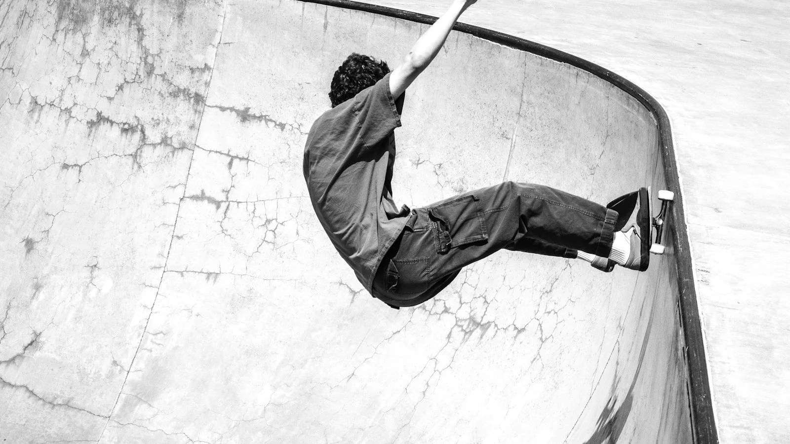 Skateboarder riding high along the curved wall of a concrete bowl.