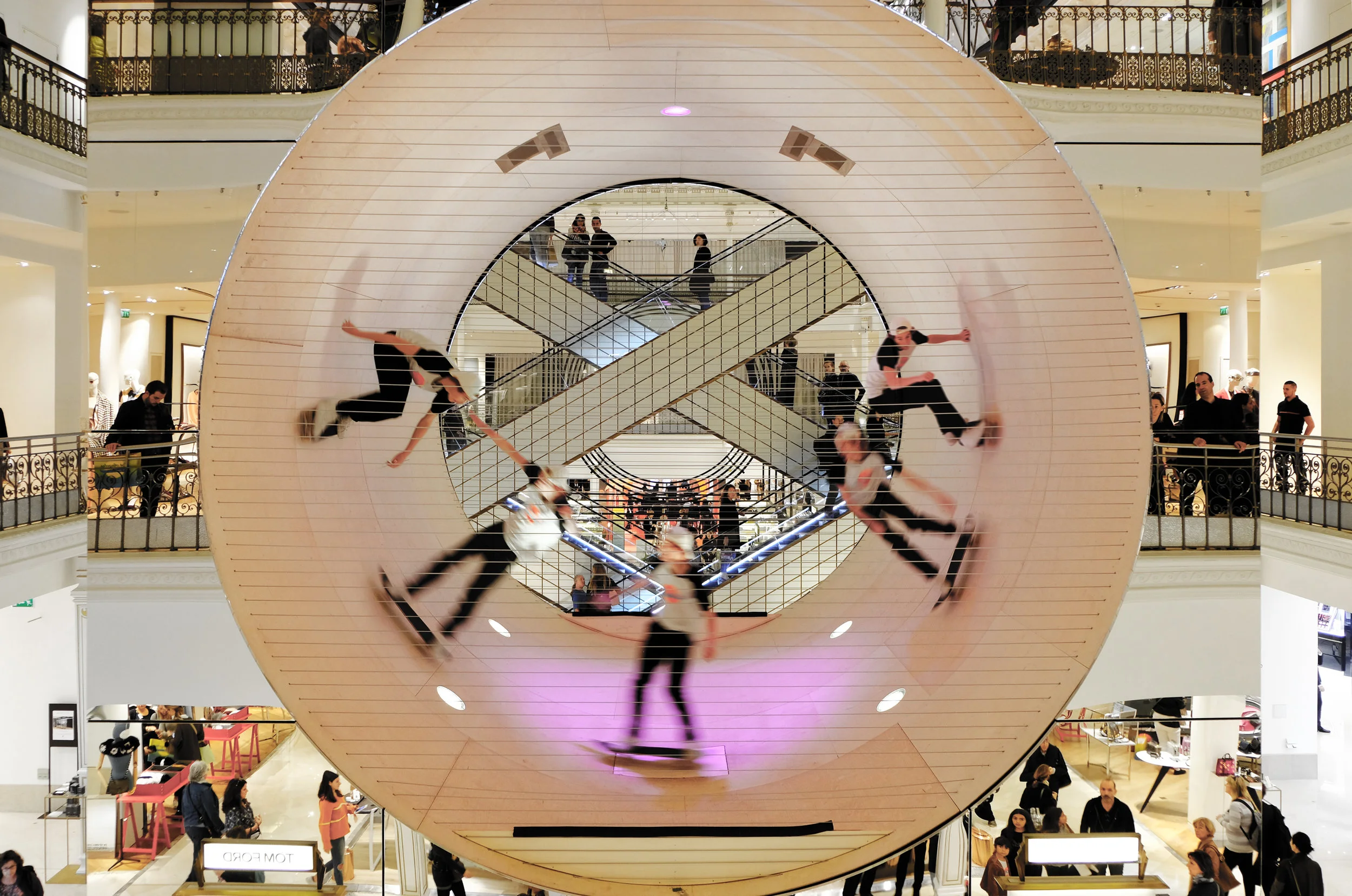 LE CUBE/ LE BON MARCHÉ/ PARIS FRANCE Le Cube, located in one of the most prominent stores in Paris, was an engaging and exciting project for shoppers and passersby. Spectators were encouraged to approach and take photos in its reflection, as well as watch the skaters perform from a multitude of angles and levels. From the first floor, an onlooker could see directly into and through the full-pipe, intimately at eye level with the elevated performer. The reflections of the interior retail space created the illusion that the full-pipe was a cylindrical void suspended within the open interior courtyard of the store. Although it did not feature a specific brand it created an extraction to the surrounding merchandise and exhibitions. Acting as centerpiece of the Los Angeles exhibit, the installation did not merely showcase the city’s fashion and beauty products, but more so the city’s underlying influences. Le Cube was a nod to street culture. Local skaters were given a platform to have fun and perform, and they did not disappoint. Le Cube’s spotlights and speakers highlighted their abilities. For Scott Oster, Le Cube was a passion project, one that drew upon his experience as a designer and professional skater. For John Manaves AIA and MANA architects, it was an opportunity to focus on detailing and the process of fabrication. The smallest of elements were considered in the design and ultimately realized by the Le Bon Marché team. Upon inspection, one would have a difficult time locating the access door in the base, the safety wires protecting the ramp openings or the ramp’s hatch door were all carefully concealed. Particular time was spent on providing sleek and intentional seams between panels, as well as efficient use of structure by the Endrestudio engineering team. Le Cube acted as a thought-provoking intersection between sport and sculptural art. When a performance was occurring inside, the atmosphere was dynamic and stimulating. When it was not being activated, Le Cube sat quietly, luminously reflecting the architecture of its surroundings—warm lights, decorative iron handrails, and the famous crossing escalators of Le Bon Marché. In summary, Le Cube was conscious of its context, meticulously detailed, and engaged with the public in a fun and exciting way. Le Cube made a statement about how design can rethink and reposition the future of retail and its interiors.