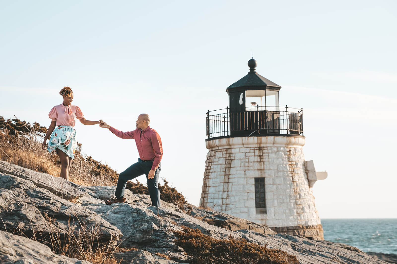  Husband helps wife down the cliff in front of Castle Hill Lighthouse in Newport, RI in celebration of their 10 year anniversary. The area has an amazing ocean view 