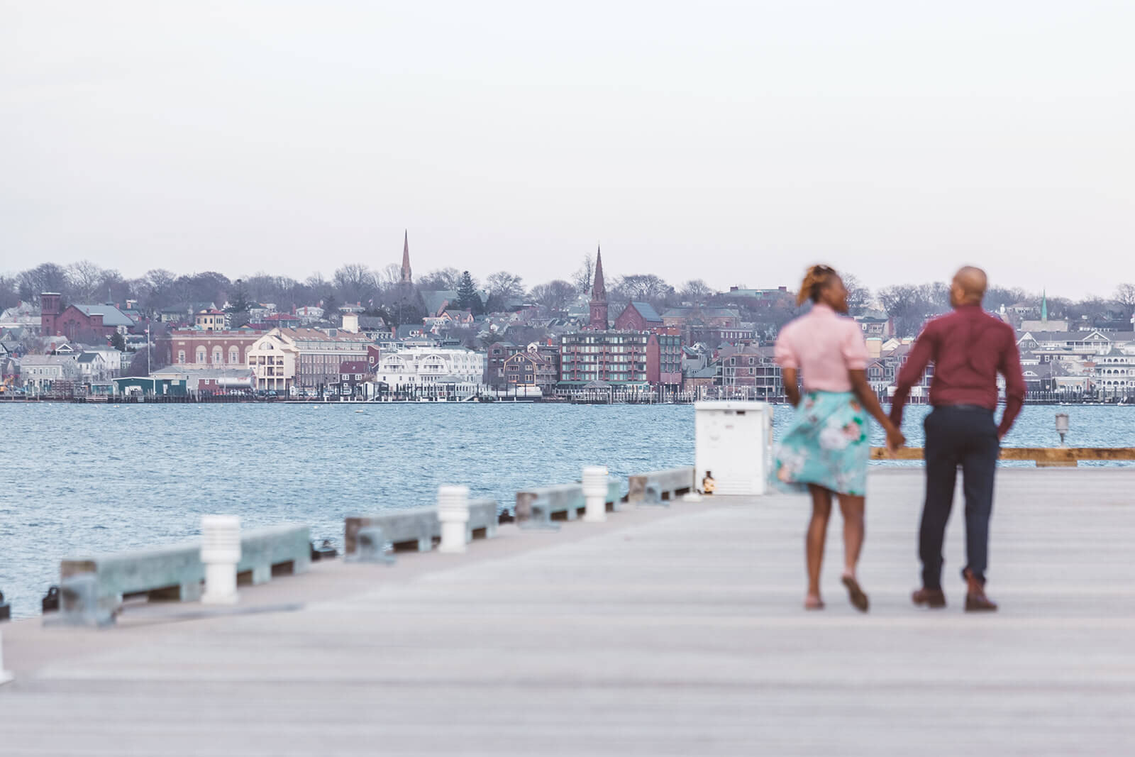  Married couple hold hands while walking down the pier at Fort Adams State Park 