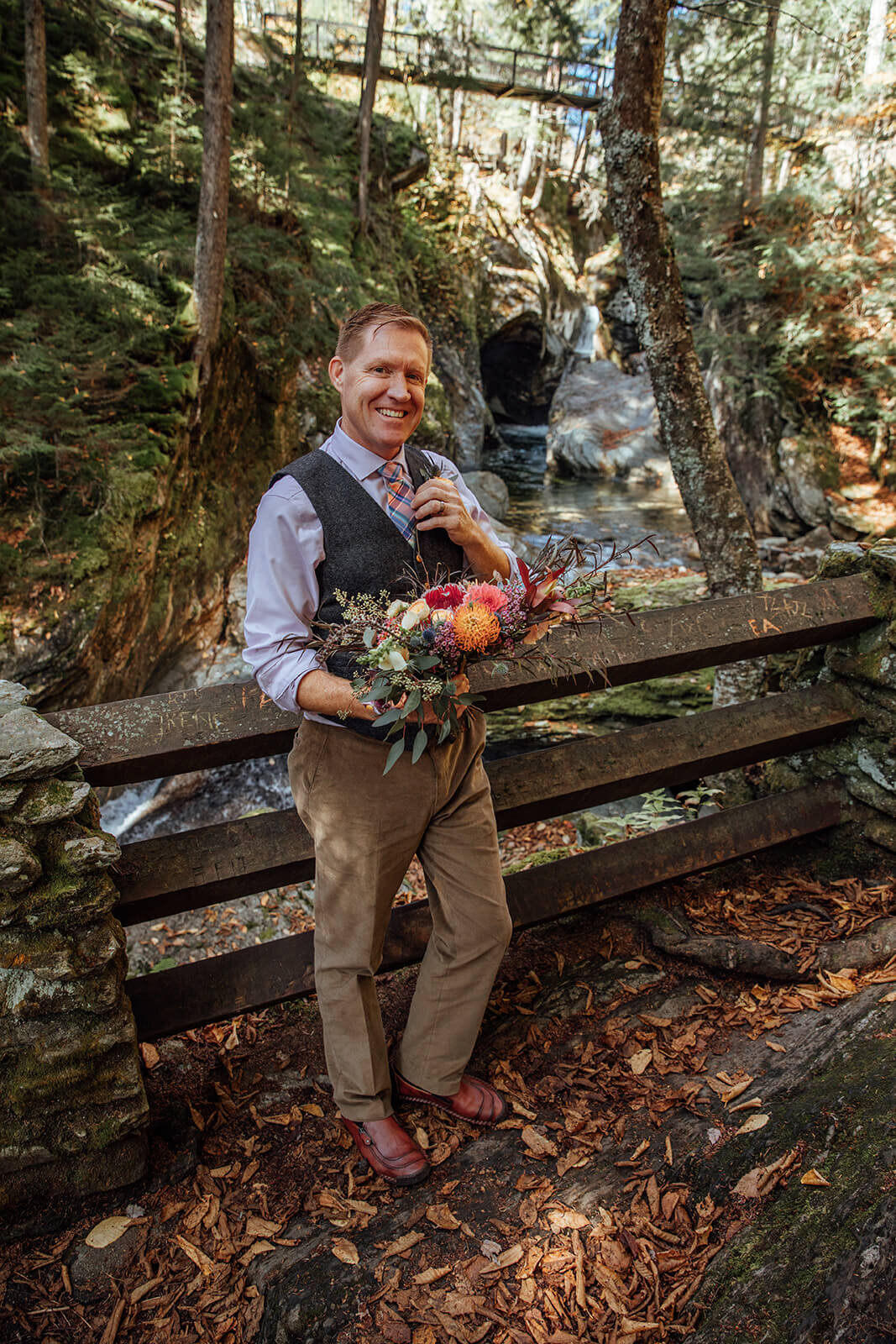  Groom holds his brides bouquet as she comes down the stairs at their Vermont elopement 