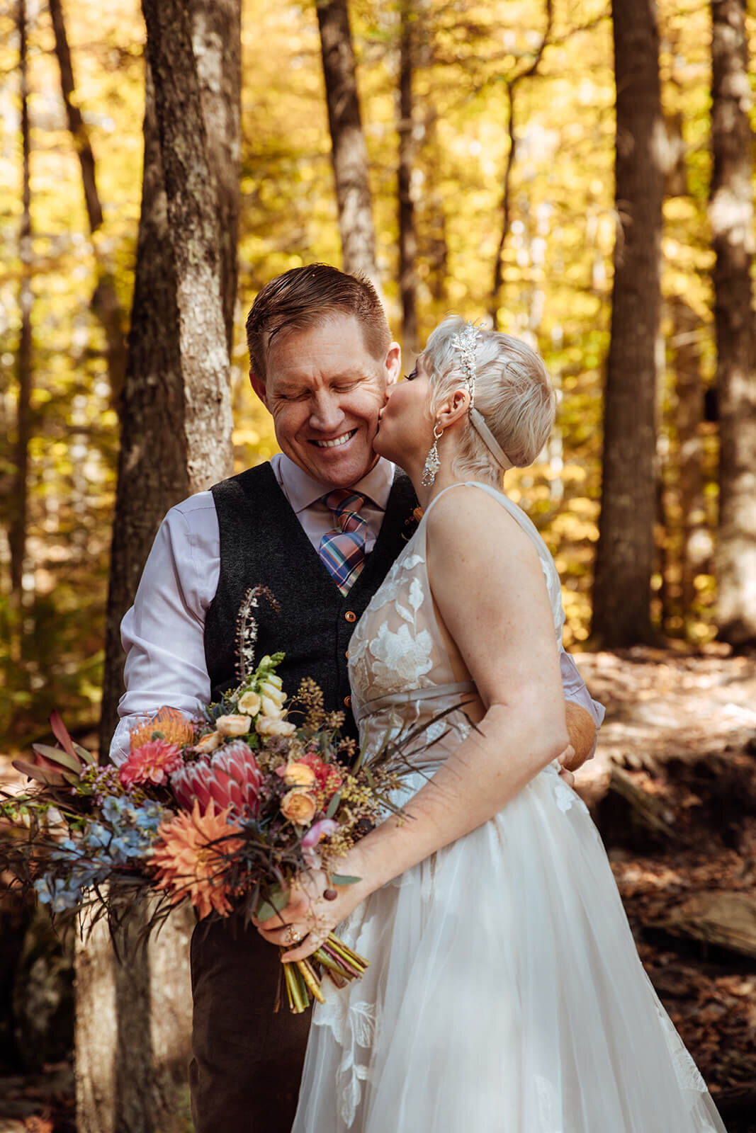  Bride kisses groom on cheek in colorful fall forest at Texas Falls Recreation Area in Vermont 