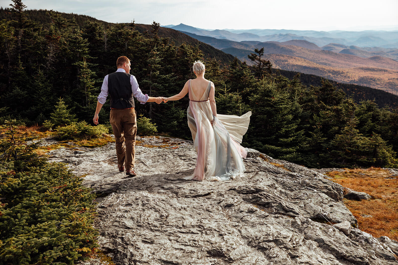  Couple holds hands and hikes along summit of Mt. Mansfield near Stowe, Vermont after their elopement 