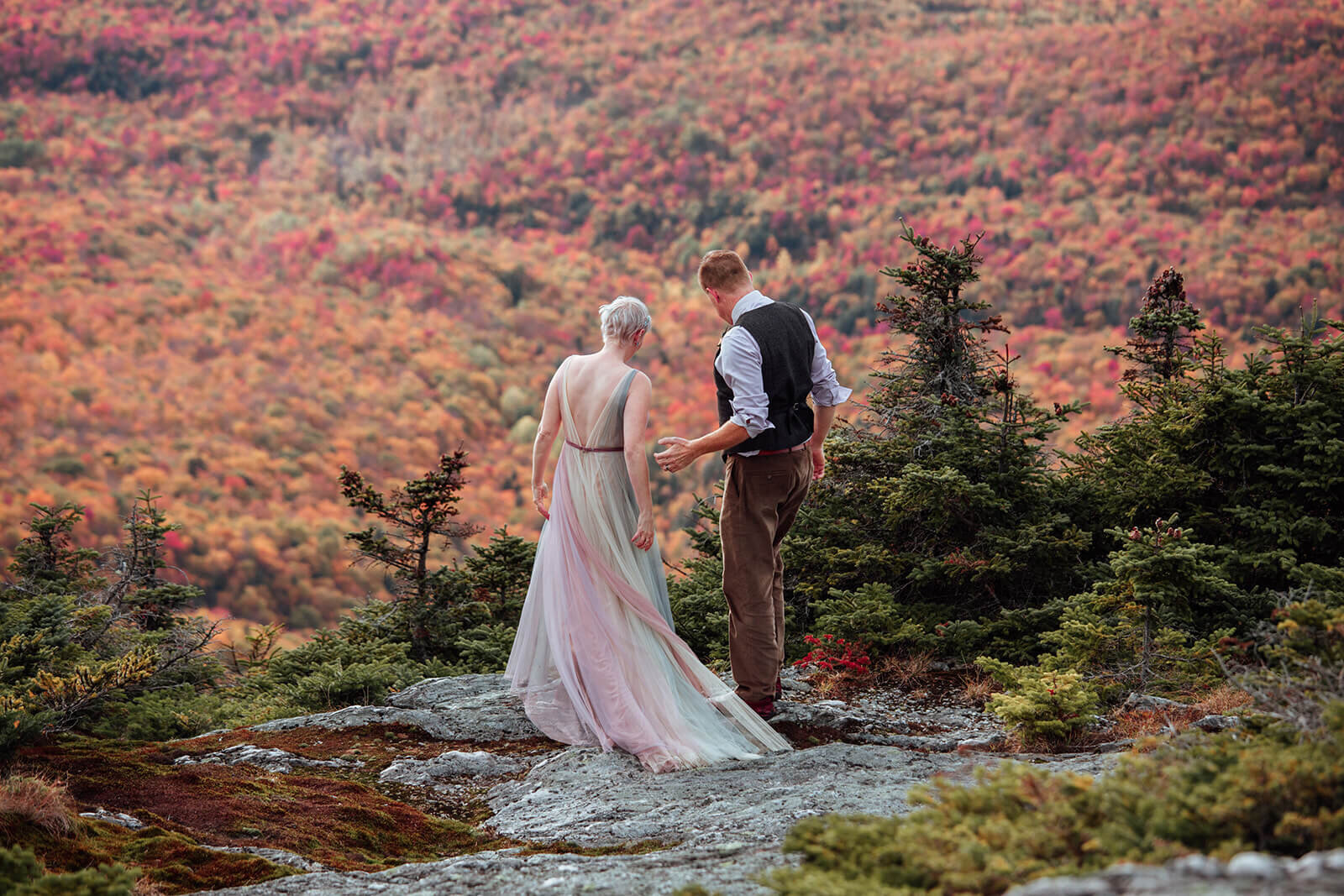  Bride in a rainbow dress and  groom enjoy a look down on the foliage view from the summit of Mt. Mansfield near Stowe, Vermont after their elopement 