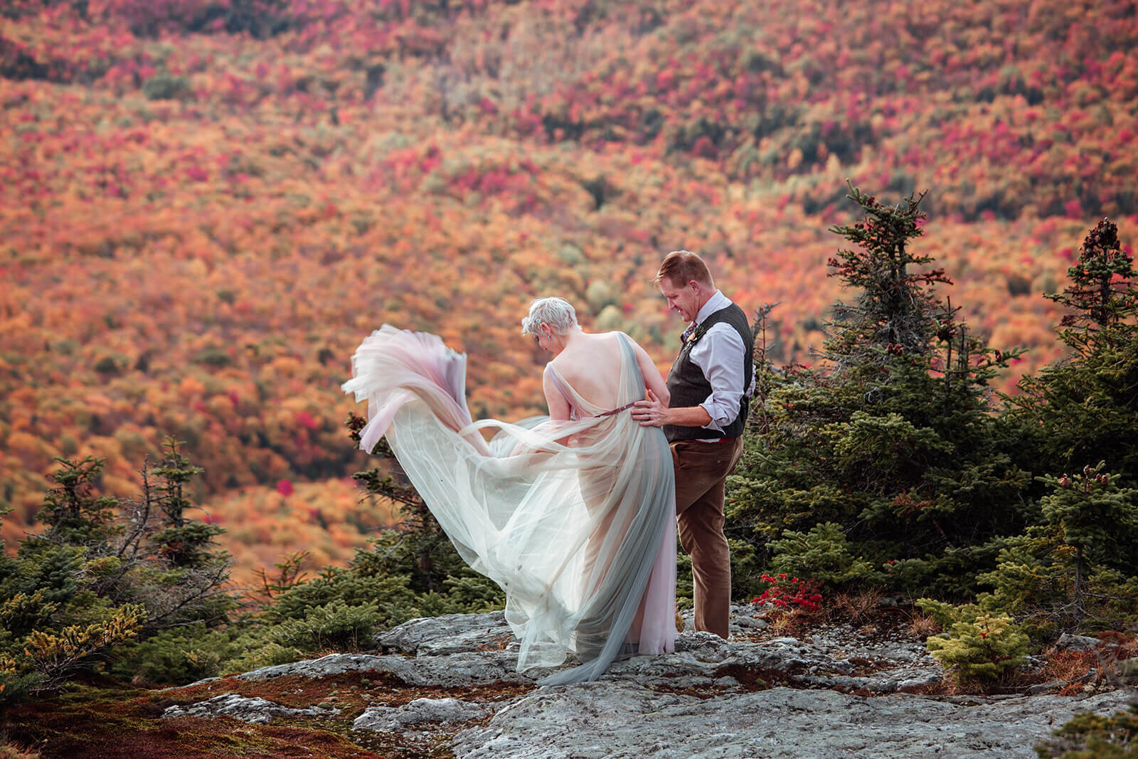  Bride in a rainbow dress and groom enjoy a look down on the foliage view from the summit of Mt. Mansfield near Stowe, Vermont after their elopement 
