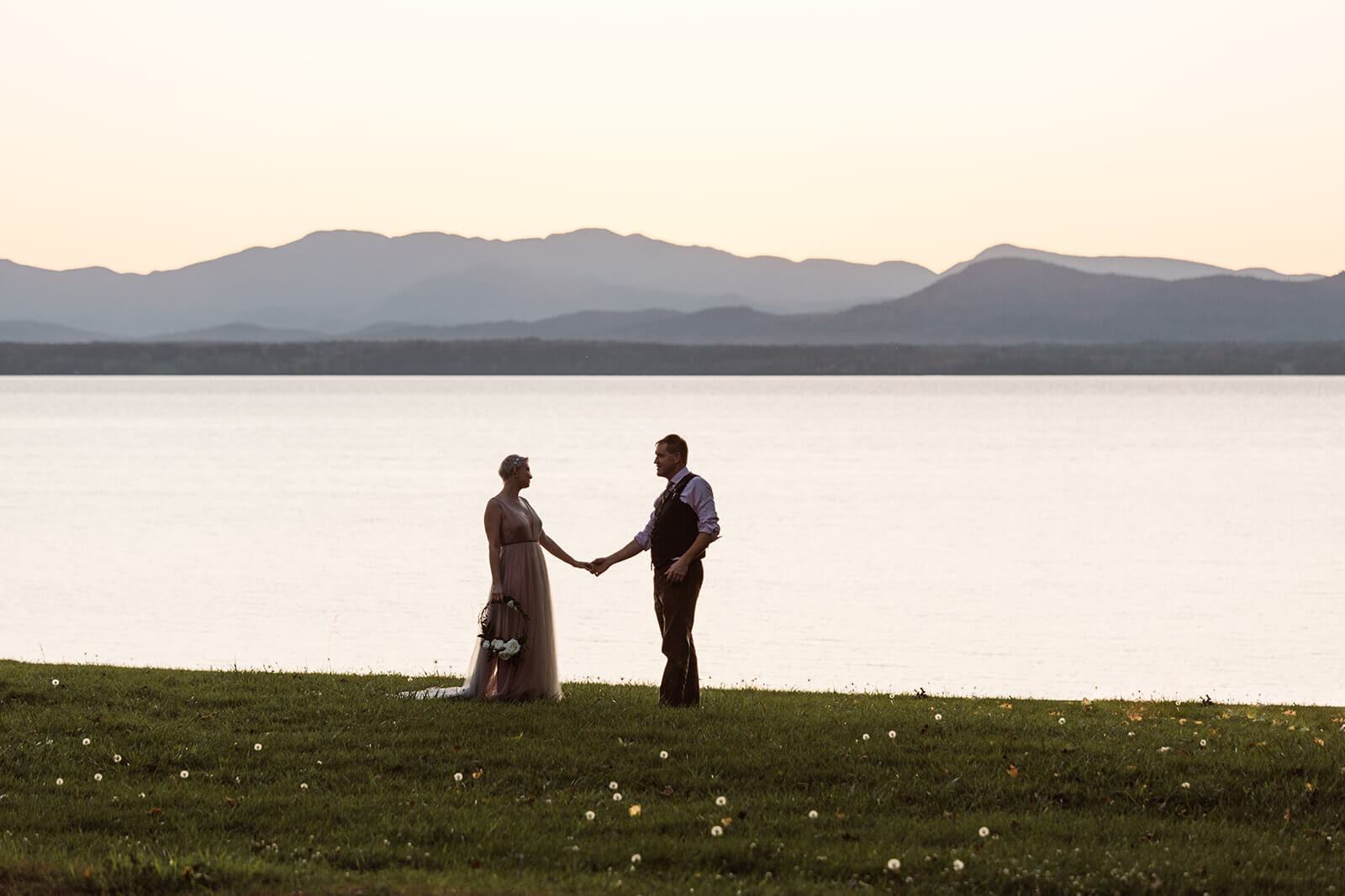  Bride and groom hold hands at sunset in front of Lake Champlain outside Burlington, Vermont after their elopement 