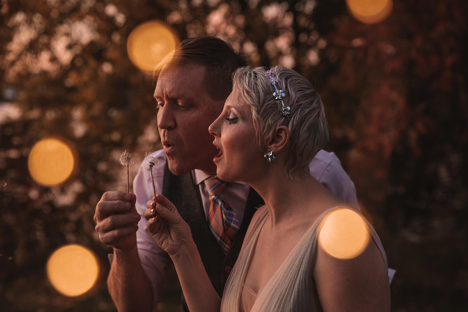  Bride and groom blowing dandelion seeds through fairy lights at Lake Champlain outside of Burlington, Vermont 