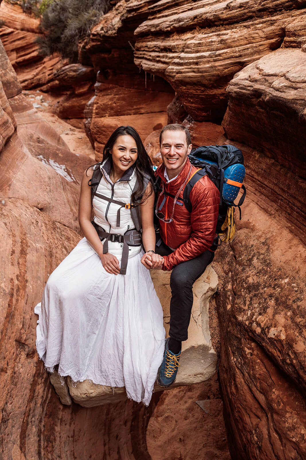  Eloping couple explore and sit on a chokestone in a technical canyon outside of Zion National Park. Zion National Park elopement photographer 