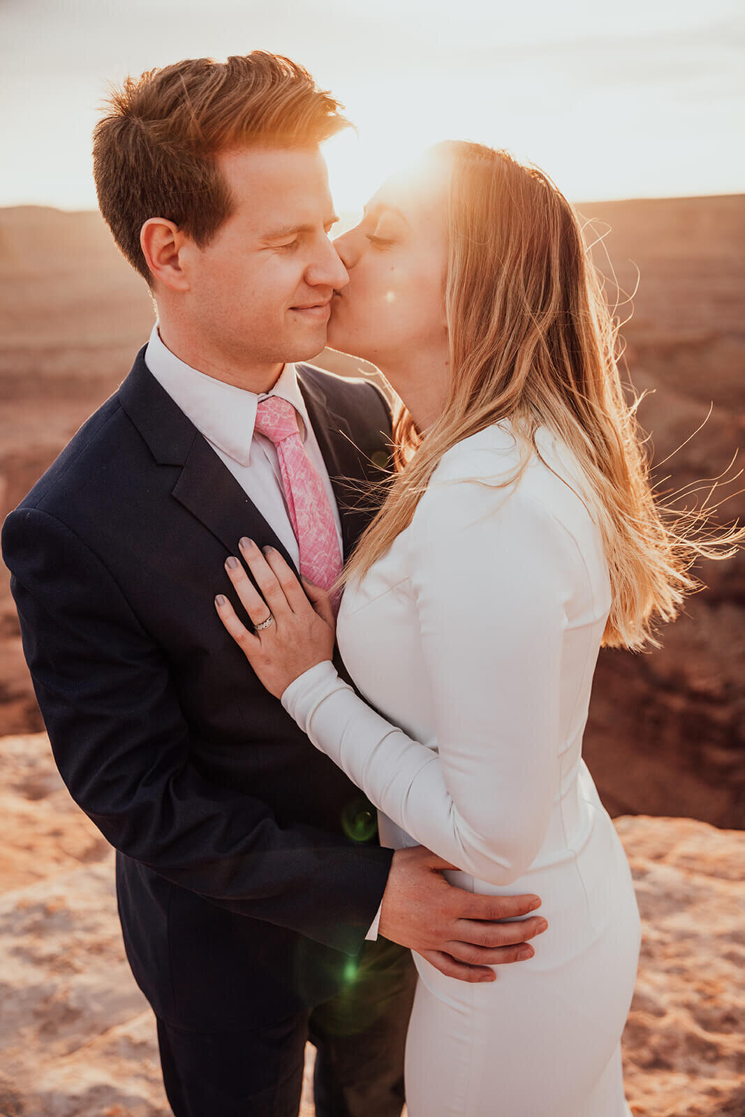  Couple celebrates anniversary and kisses during sunset at Dead Horse Point State Park and the La Sal Mountains near Moab, Utah with incredible views and hiking. Utah elopement photographer 