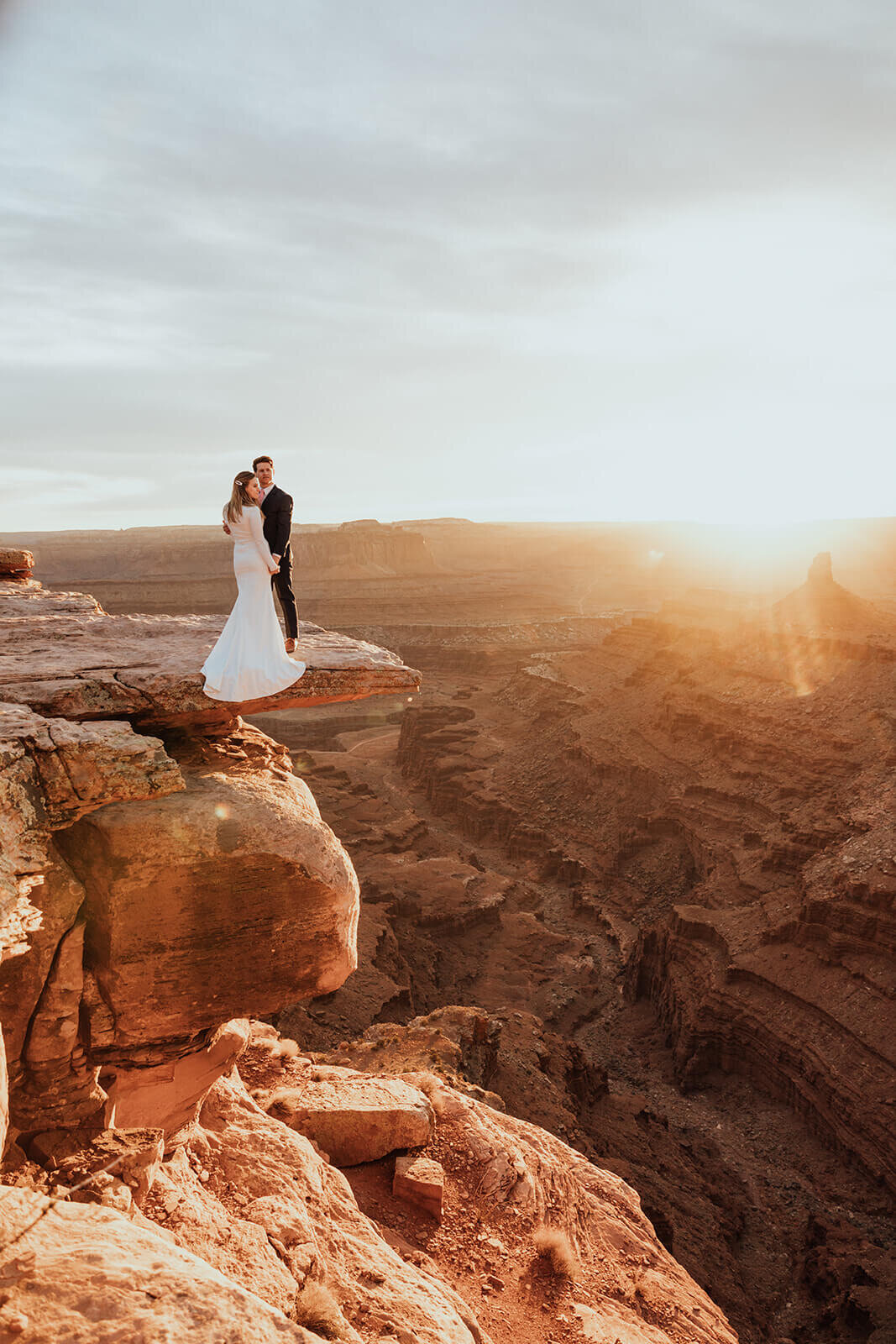  Couple celebrates anniversary and kisses during sunset at Dead Horse Point State Park and the La Sal Mountains near Moab, Utah with incredible views and hiking. Utah elopement photographer 