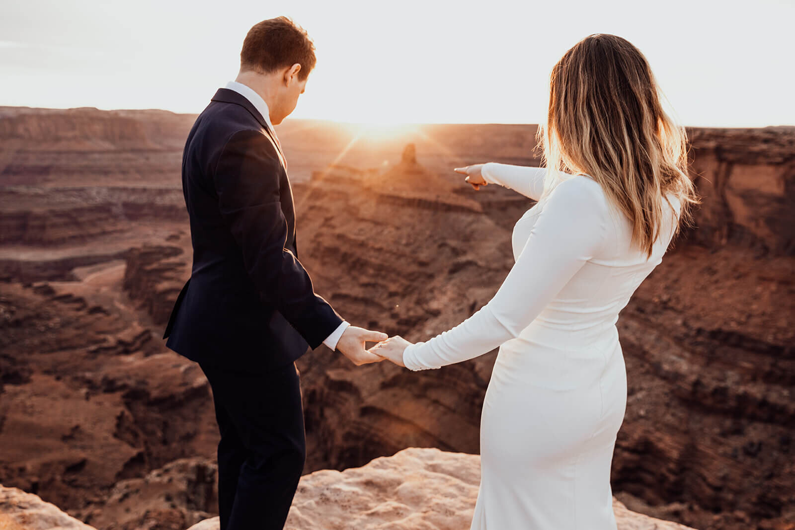  Couple looks at desert towers while celebrating anniversary during sunset at Dead Horse Point State Park and the La Sal Mountains near Moab, Utah with incredible views and hiking. Utah elopement photographer 