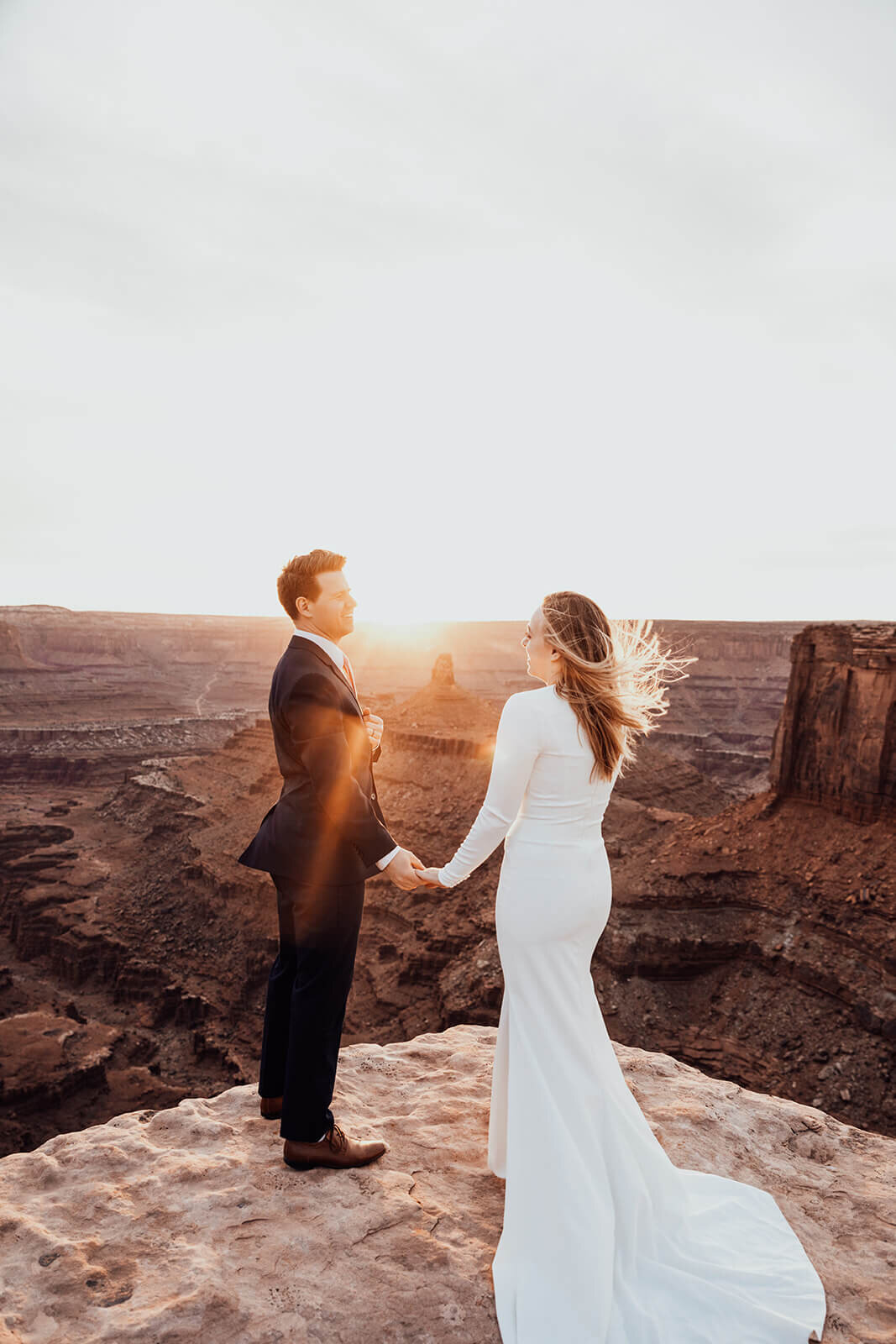  Couple looks at desert towers while celebrating anniversary during sunset at Dead Horse Point State Park and the La Sal Mountains near Moab, Utah with incredible views and hiking. Utah elopement photographer 