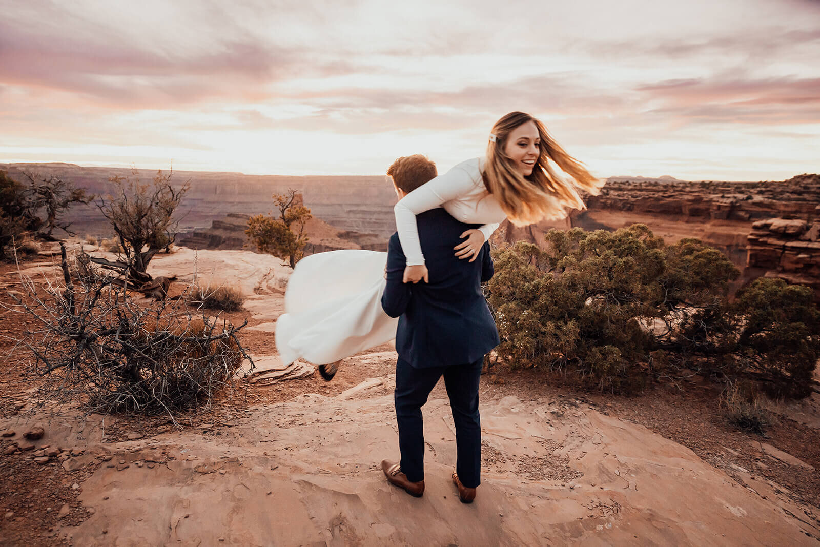  Groom throws bride over his shoulders during elopement at Dead Horse Point State park. Moab elopement photographer 