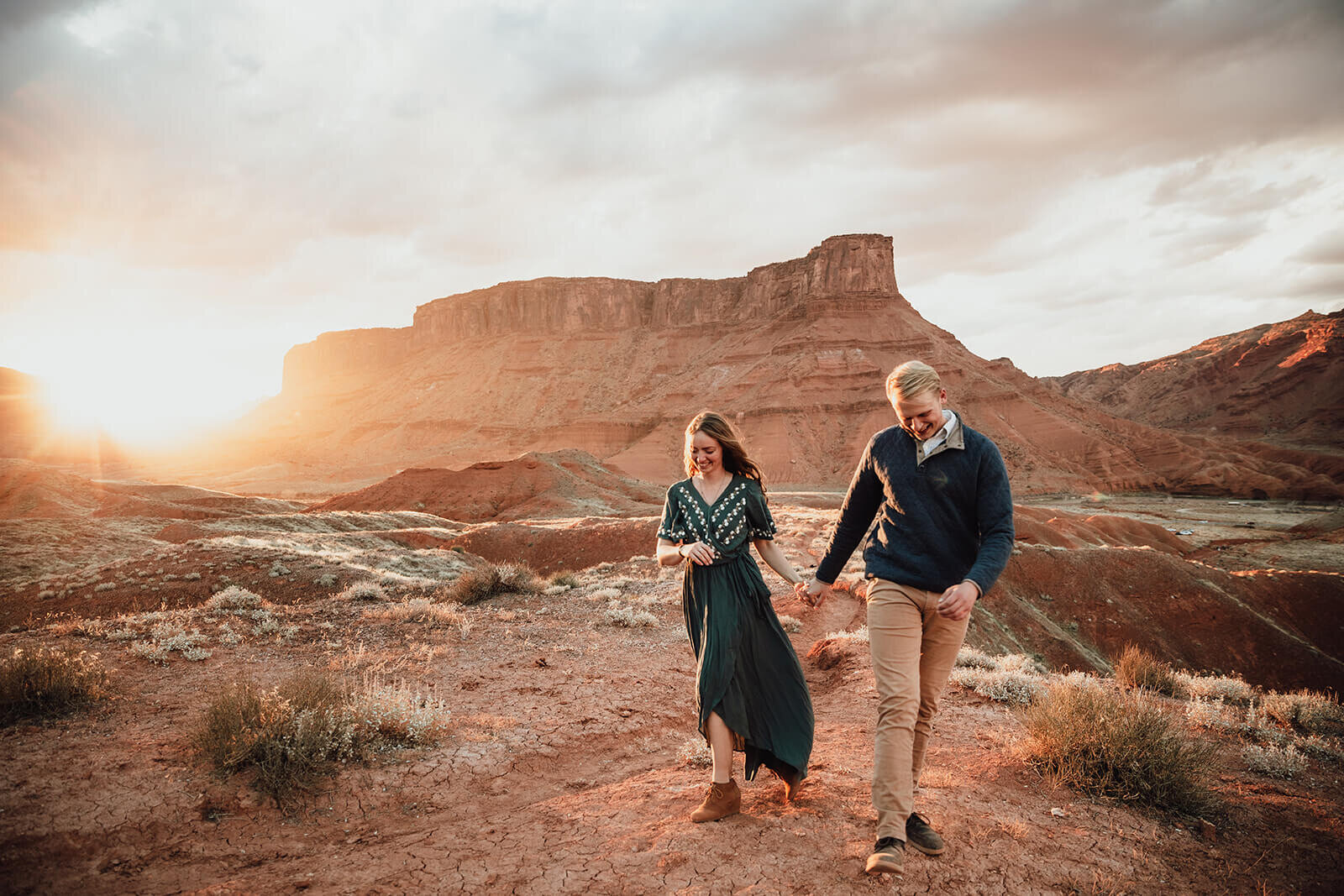  Couple are playful in the setting sun in front of desert towers on public lands outside of Moab, Utah. Desert southwest elopement photographer 