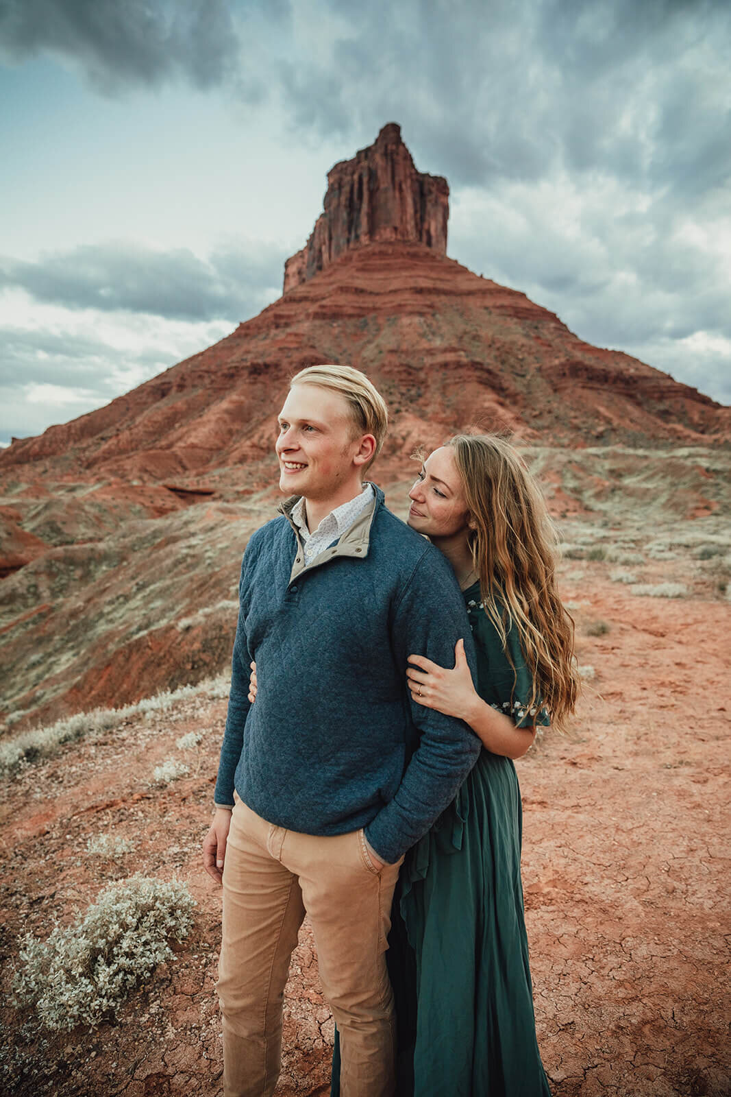  Couple are playful in the setting sun in front of desert towers on public lands outside of Moab, Utah. Desert southwest couples photographer 