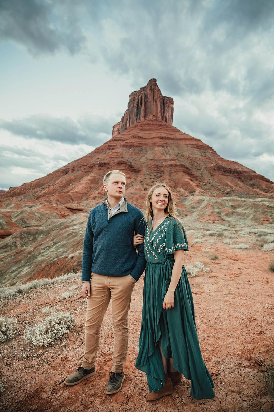  Couple are playful in the setting sun in front of desert towers on public lands outside of Moab, Utah. Desert southwest engagement photographer 