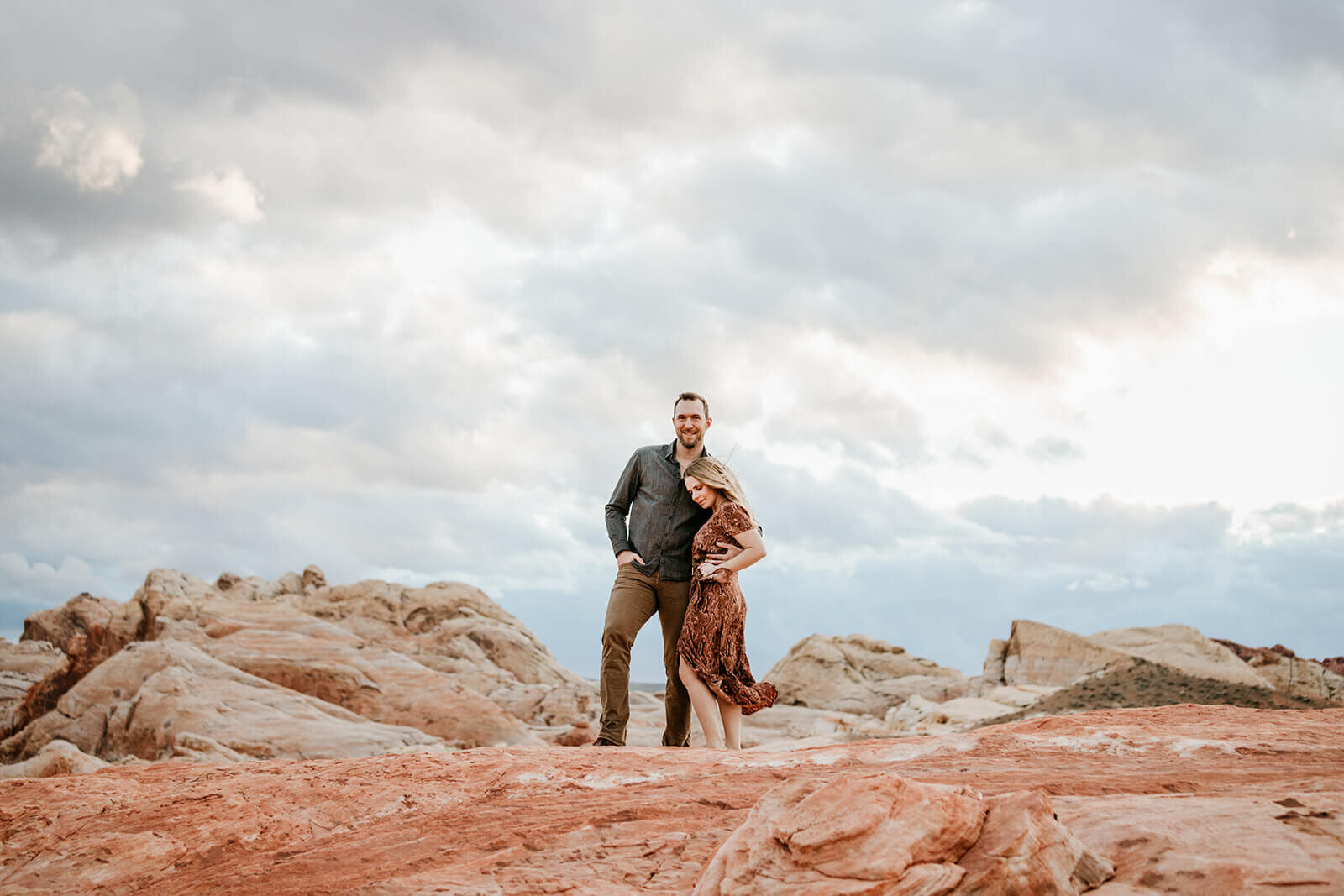  Couple watches the sunset during hike to the Fire Wave in Valley of Fire State Park next to Lake Mead, outside of Las Vegas, Nevada. Las Vegas engagement photographer 