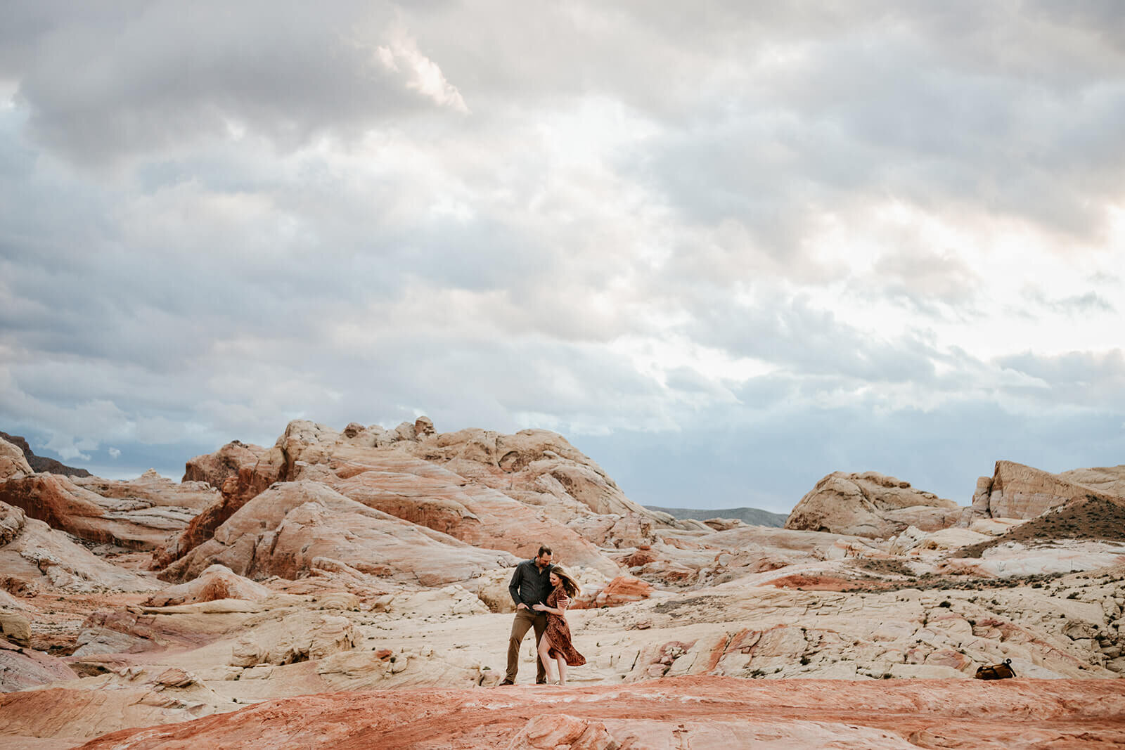  Couple watches the sunset during hike to the Fire Wave in Valley of Fire State Park next to Lake Mead, outside of Las Vegas, Nevada. Las Vegas engagement photographer 