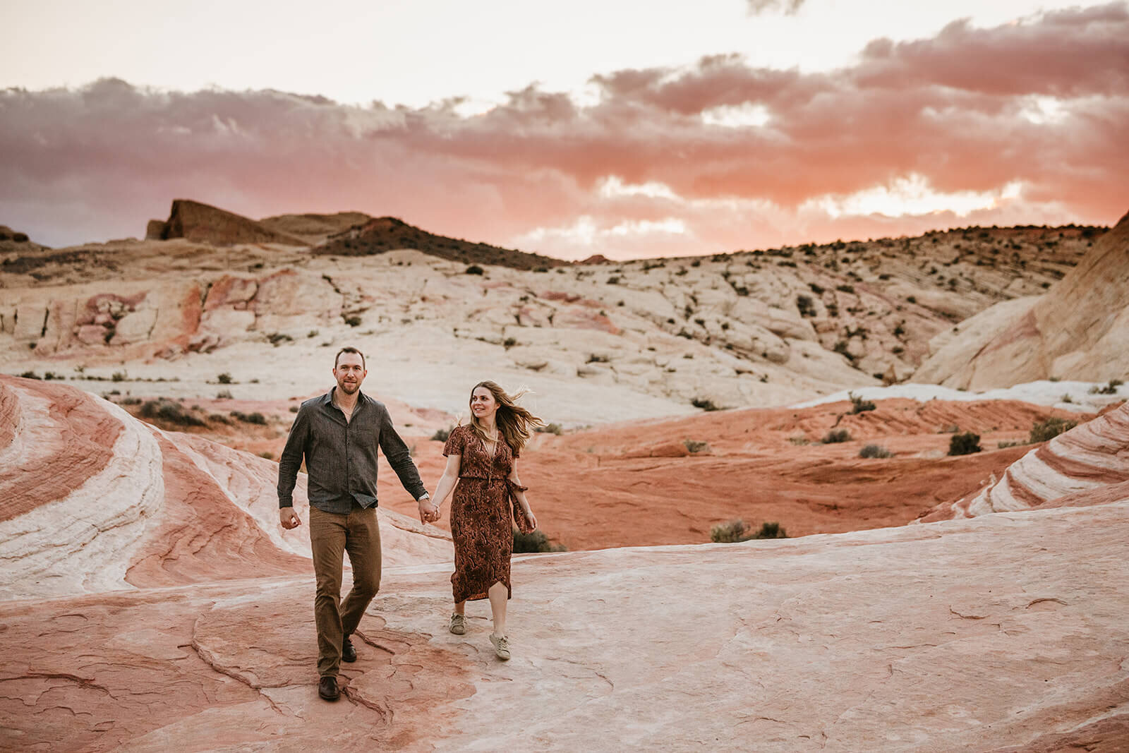  Couple watches the sunset during hike to the Fire Wave in Valley of Fire State Park next to Lake Mead, outside of Las Vegas, Nevada. Las Vegas engagement photographer 