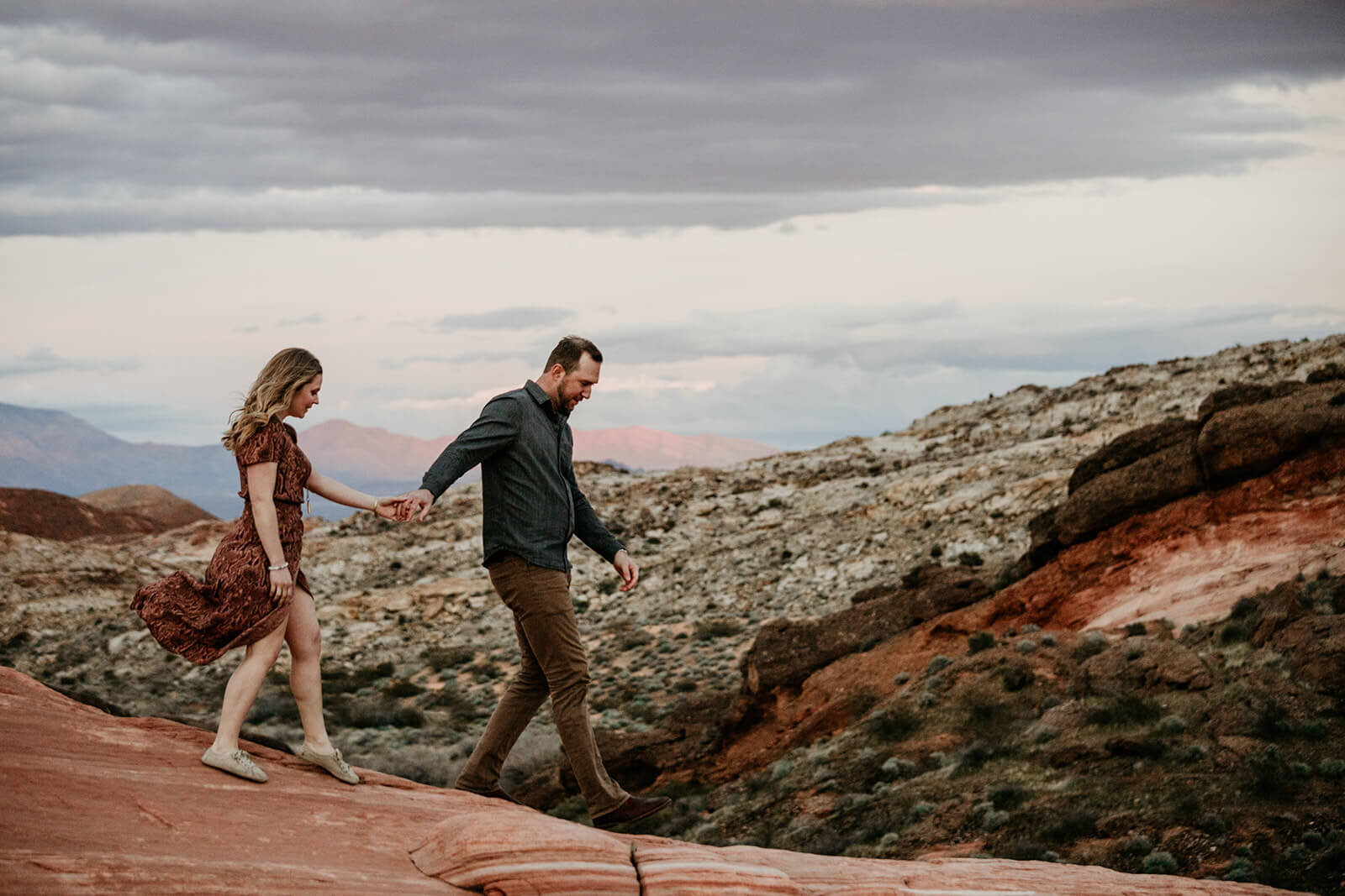 Couple watches the sunset during hike to the Fire Wave in Valley of Fire State Park next to Lake Mead, outside of Las Vegas, Nevada. Las Vegas engagement photographer 