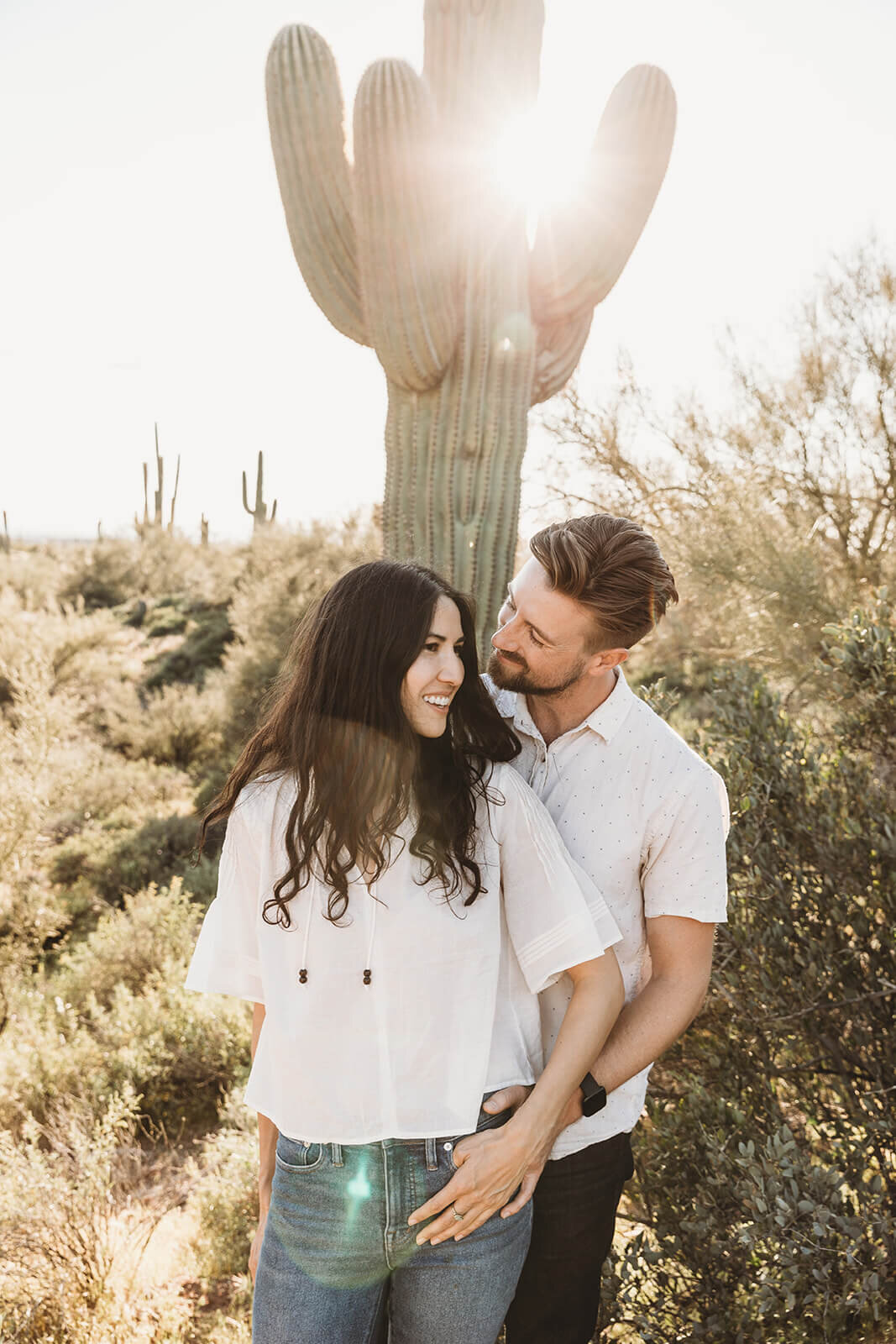  Couple snuggles by saguaro cactus during engagement session in the Superstition Mountains outside of Phoenix, Arizona. Arizona elopement photographer 