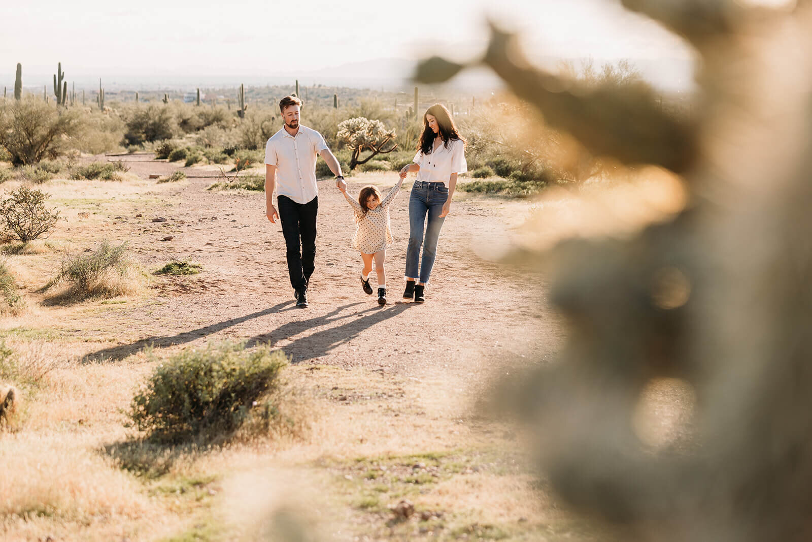  Little girl holds parents hands during their engagement session in the Superstition Mountains outside of Phoenix, Arizona. Arizona elopement photographer 