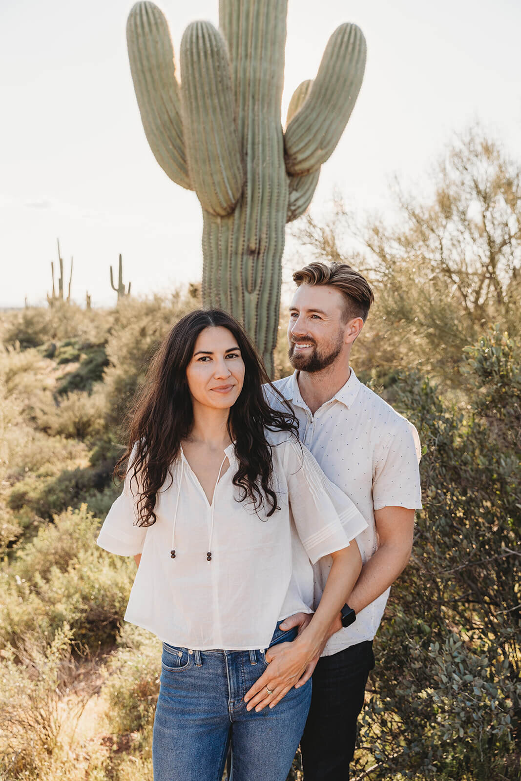  Couple snuggles by saguaro cactus during engagement session in the Superstition Mountains outside of Phoenix, Arizona. Arizona elopement photographer 