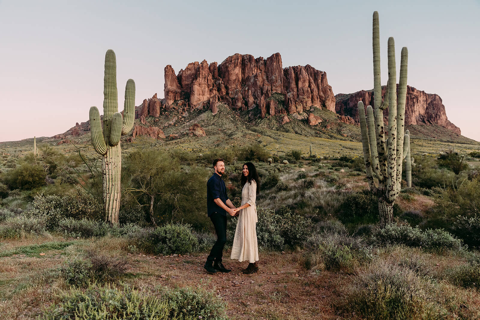  Couple hikes through desert wonderland during sunset during their engagement session in the Superstition Mountains outside of Phoenix, Arizona. Phoenix elopement photographer 