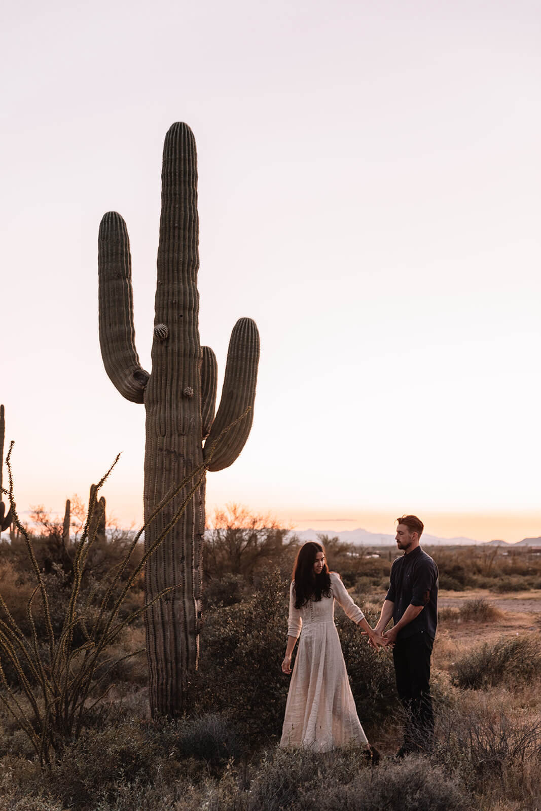  Couple hikes through desert wonderland during sunset during their engagement session in the Superstition Mountains outside of Phoenix, Arizona. Phoenix elopement photographer 