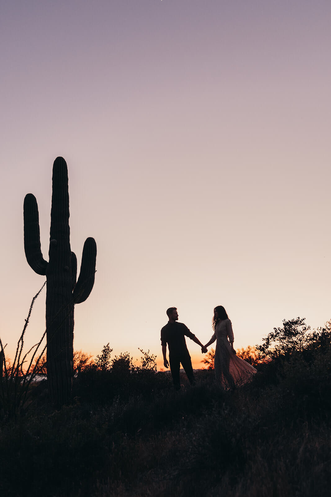  Couple hikes through desert wonderland during sunset during their engagement session in the Superstition Mountains outside of Phoenix, Arizona. Phoenix elopement photographer 