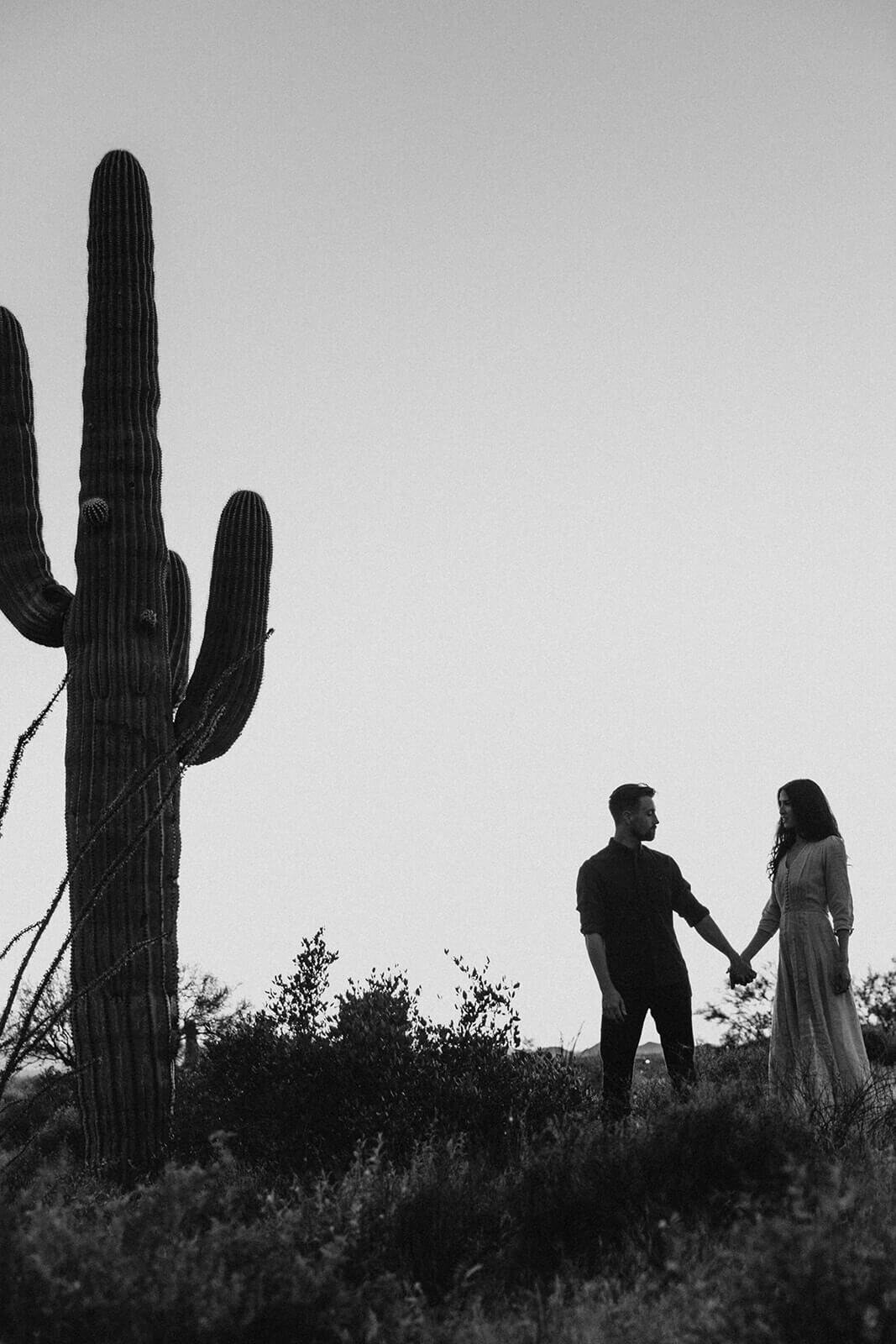  Couple hikes through desert wonderland during sunset during their engagement session in the Superstition Mountains outside of Phoenix, Arizona. Arizona elopement photographer 