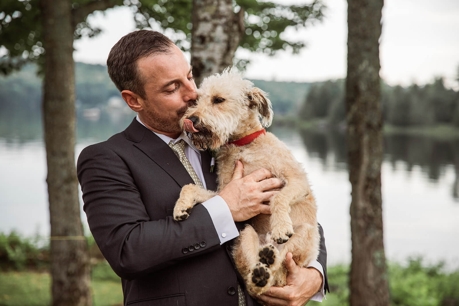  Groom kisses his dog during Maine elopement on a lake. 