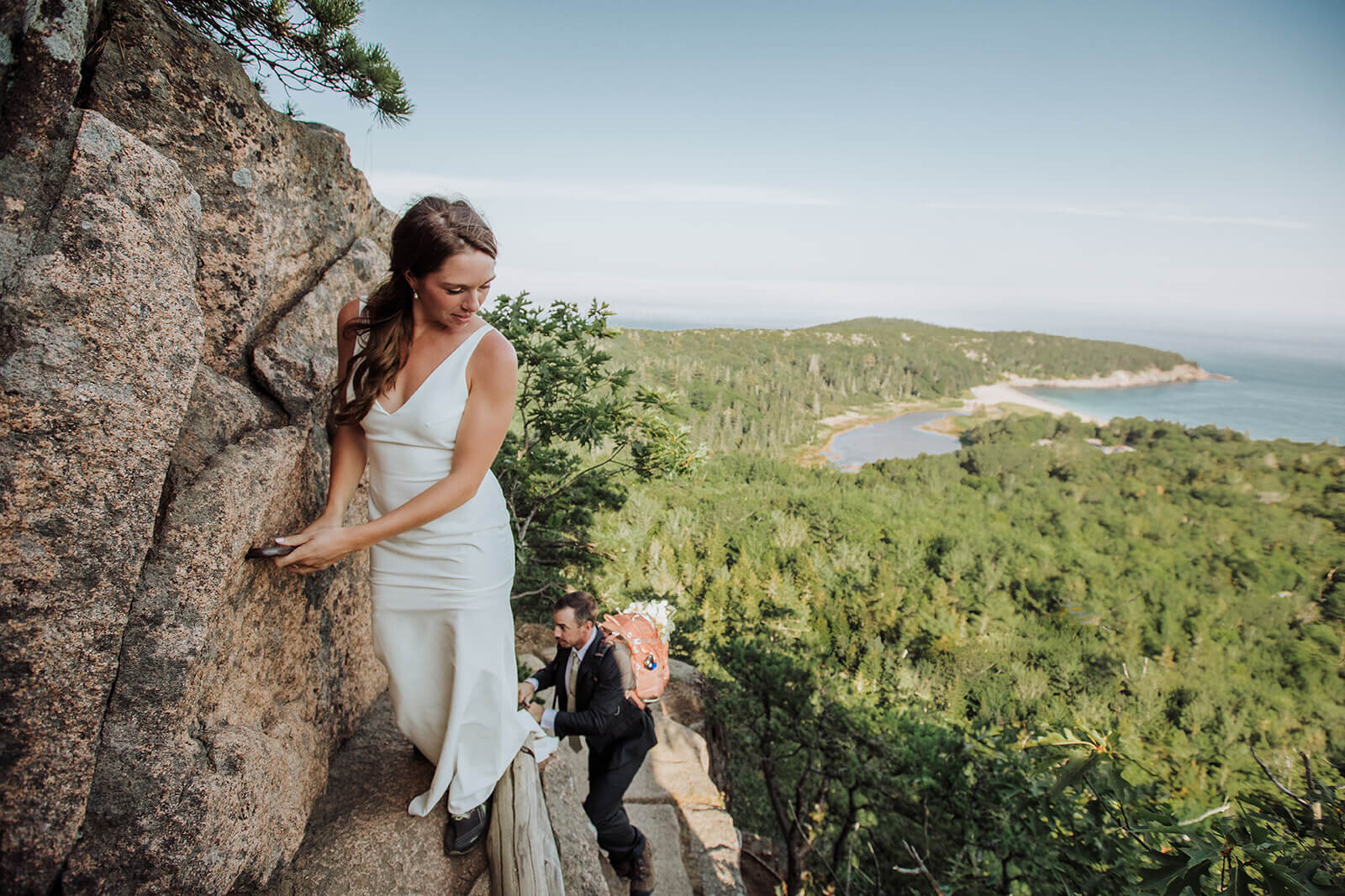  Eloping couple climbs the Beehive in Acadia National Park in Maine in wedding attire. 