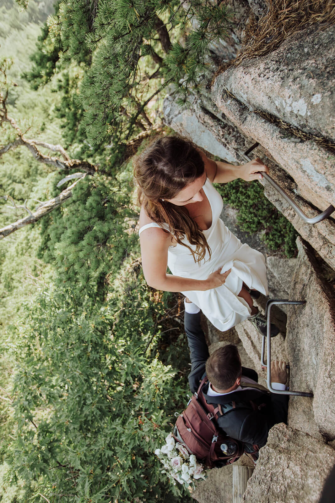  Eloping couple climbs the Beehive in Acadia National Park in Maine in wedding attire. 