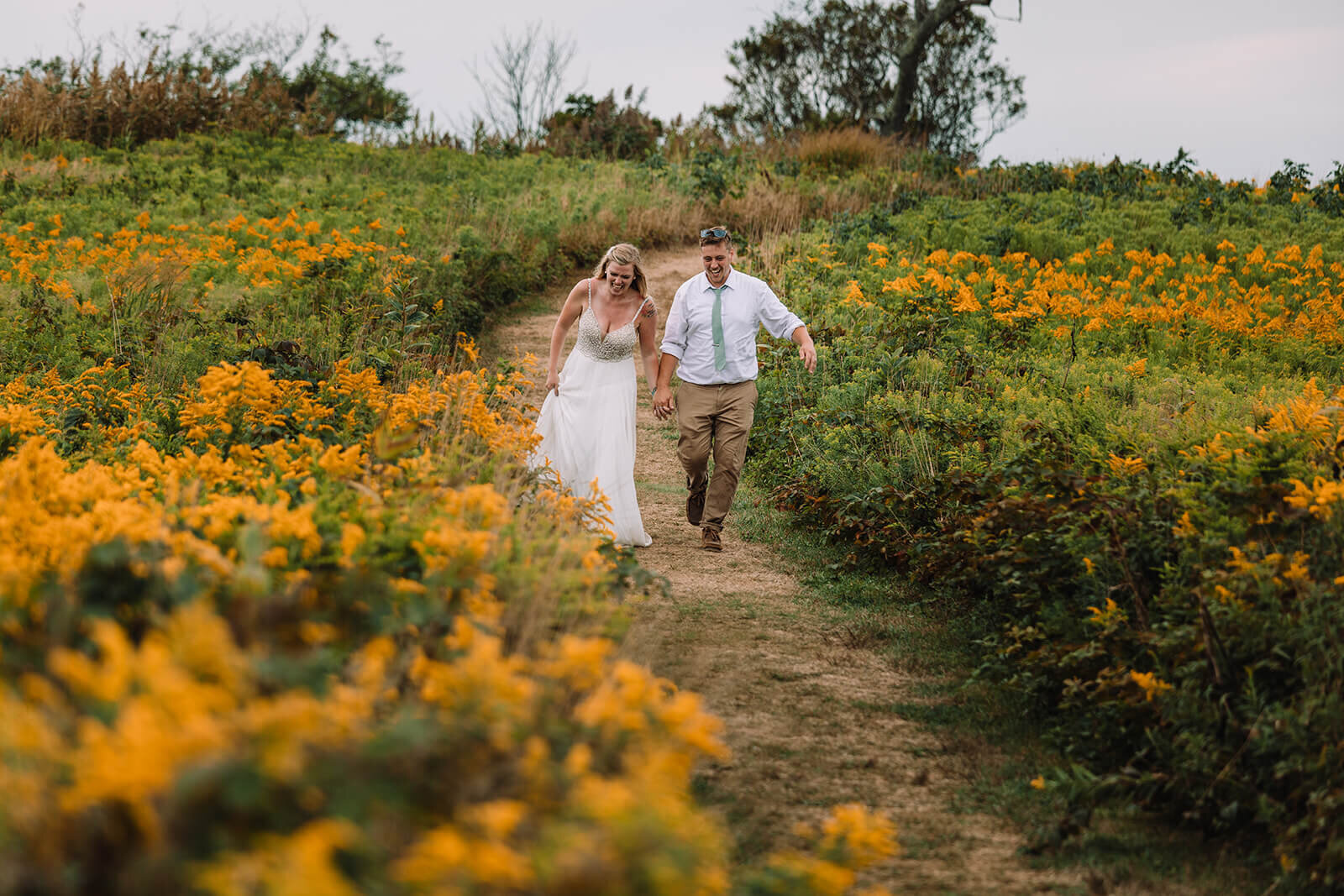  Eloping couple runs through flower fields during their hiking and beach elopement on Block Island off the coast of Rhode Island. 