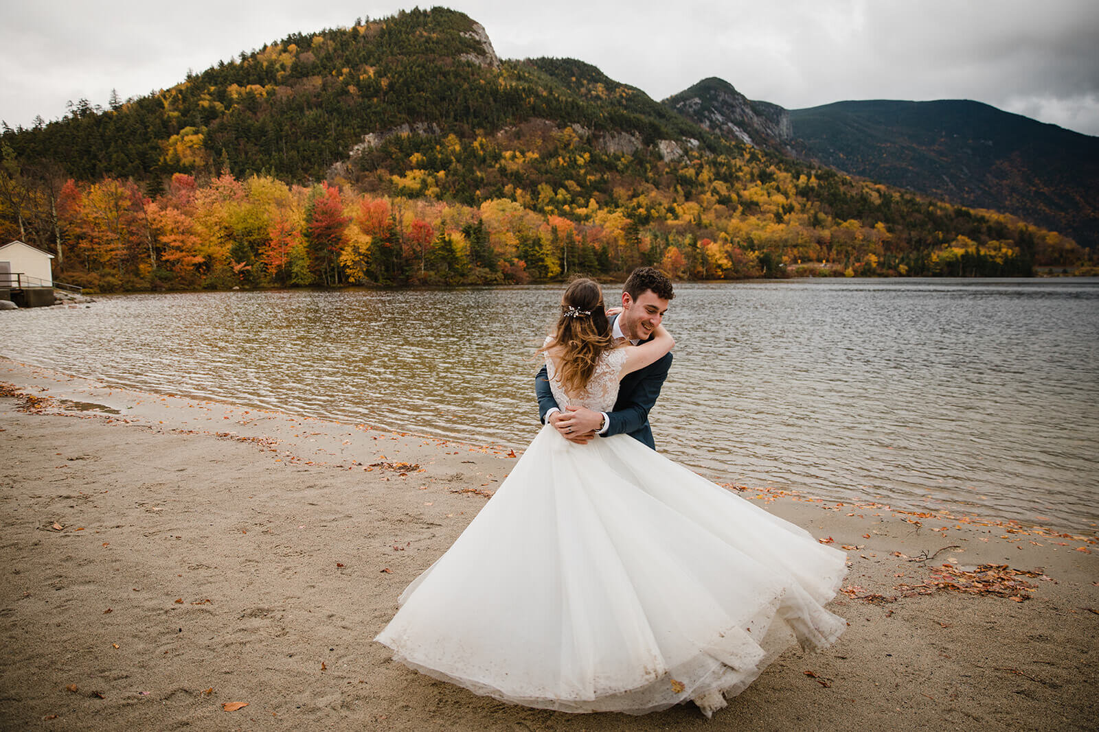  Couple explores the beach in the rainy misty weather in Franconia Notch State Park in New Hampshire after their elopement ceremony. New Hampshire elopement packages. 