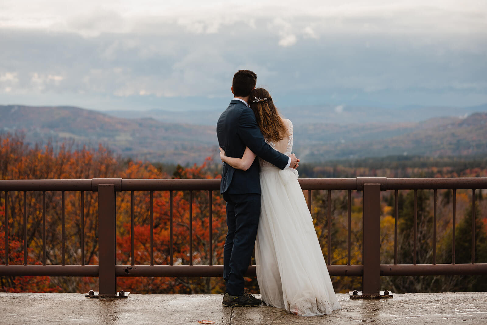  Couple explores an overlook in the rainy misty weather in Franconia Notch State Park in New Hampshire after their elopement ceremony. New Hampshire elopement packages. 