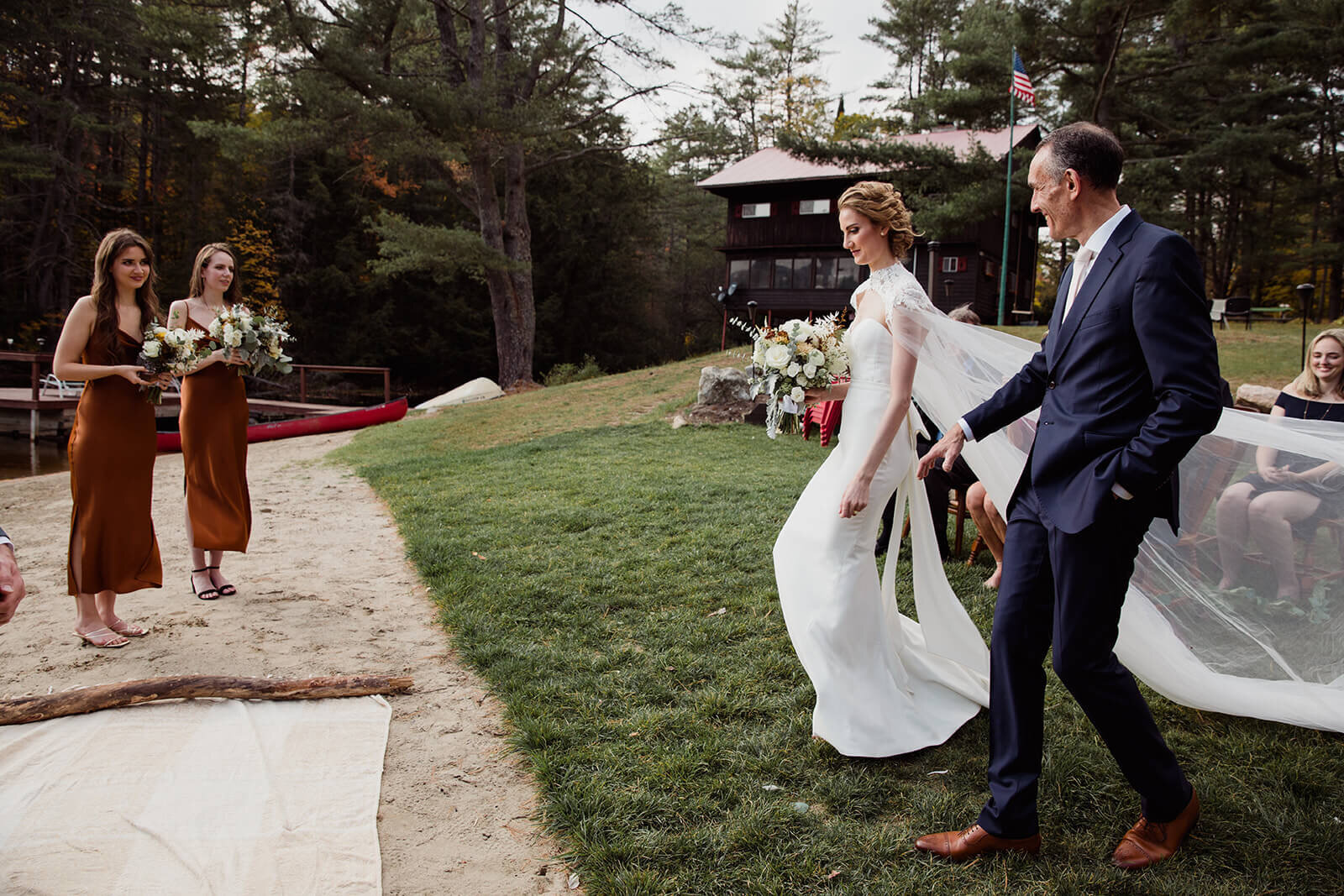  Bride walking down the aisle with her father on the lake beach during their fall wedding in the Adirondacks in Upstate New York. 