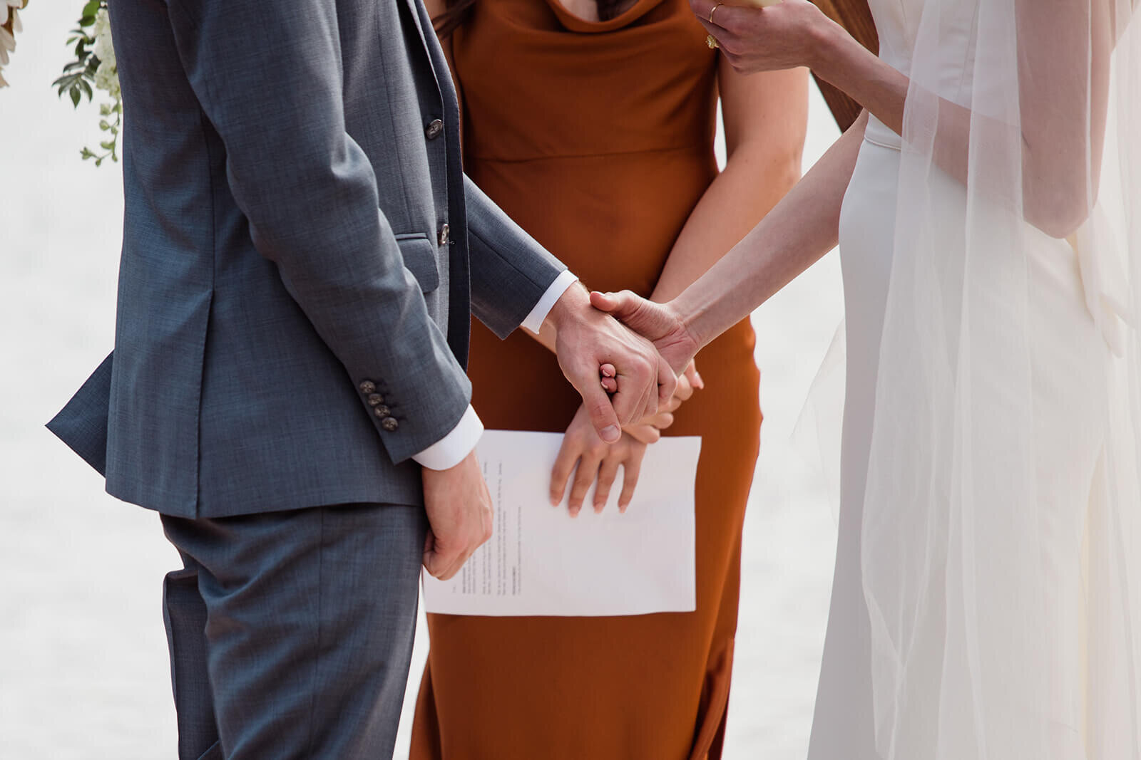  Bride and groom hold hand during the ceremony portion of their small outdoor wedding on lake beach during the fall in the Adirondacks in Upstate New York. New York wedding packages. Upstate NY elopement packages. 