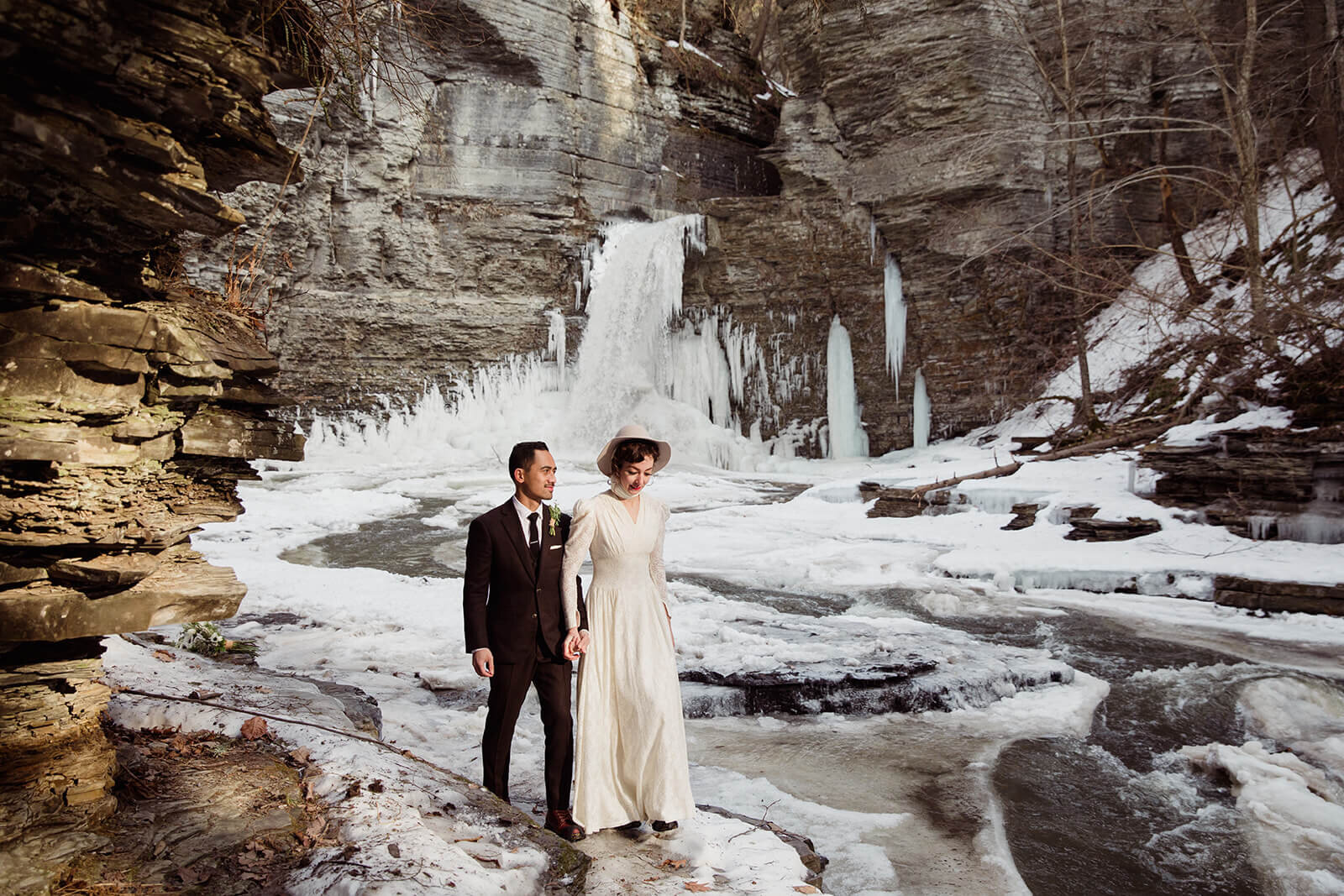  Couple hikes through frozen waterfall landscape in the Finger Lakes region of Upstate New York during their winter elopement. NY elopement packages. 