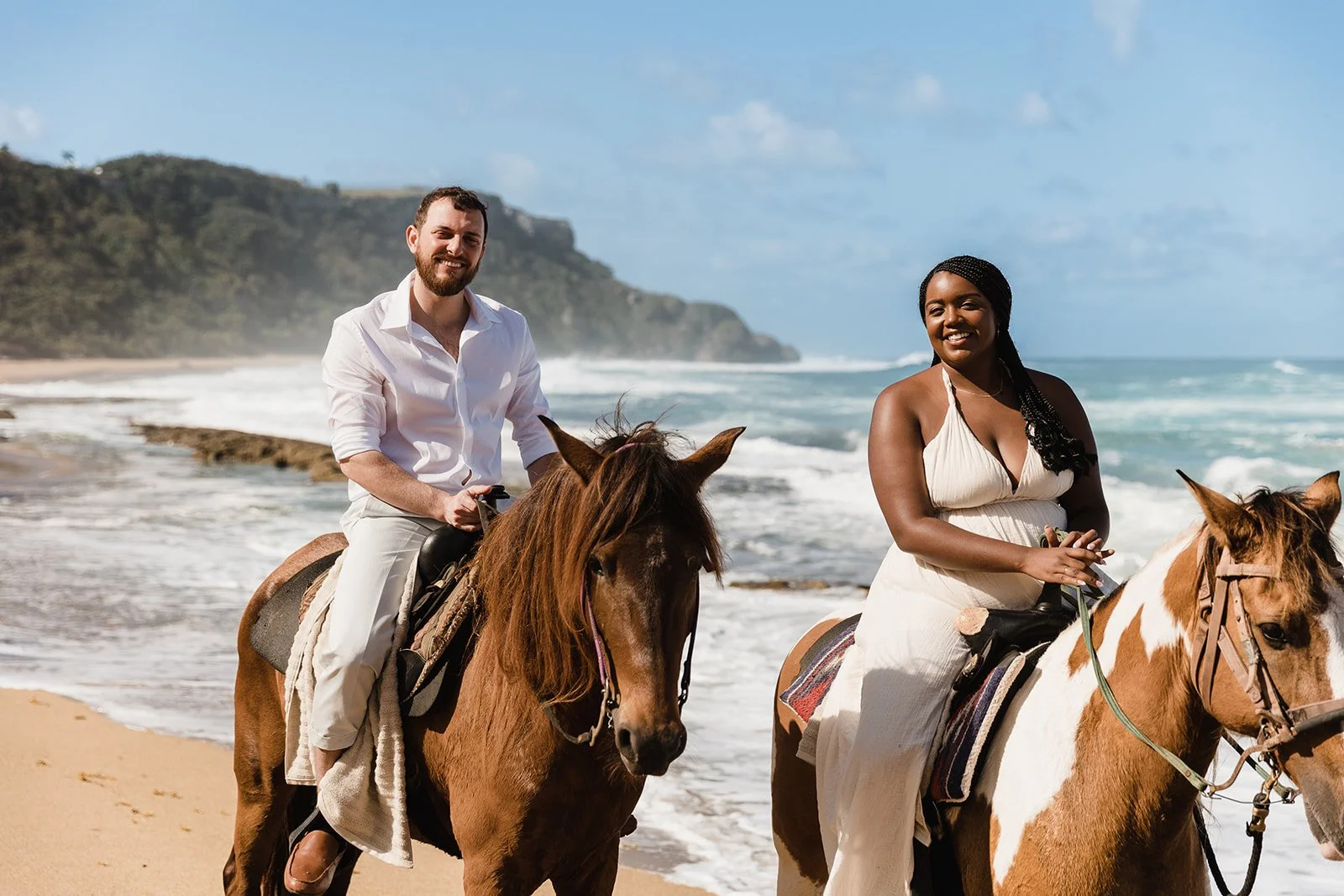 A man and woman riding horses along a sandy beach with ocean waves and cliffs in the background while eloping in Puerto Rico.