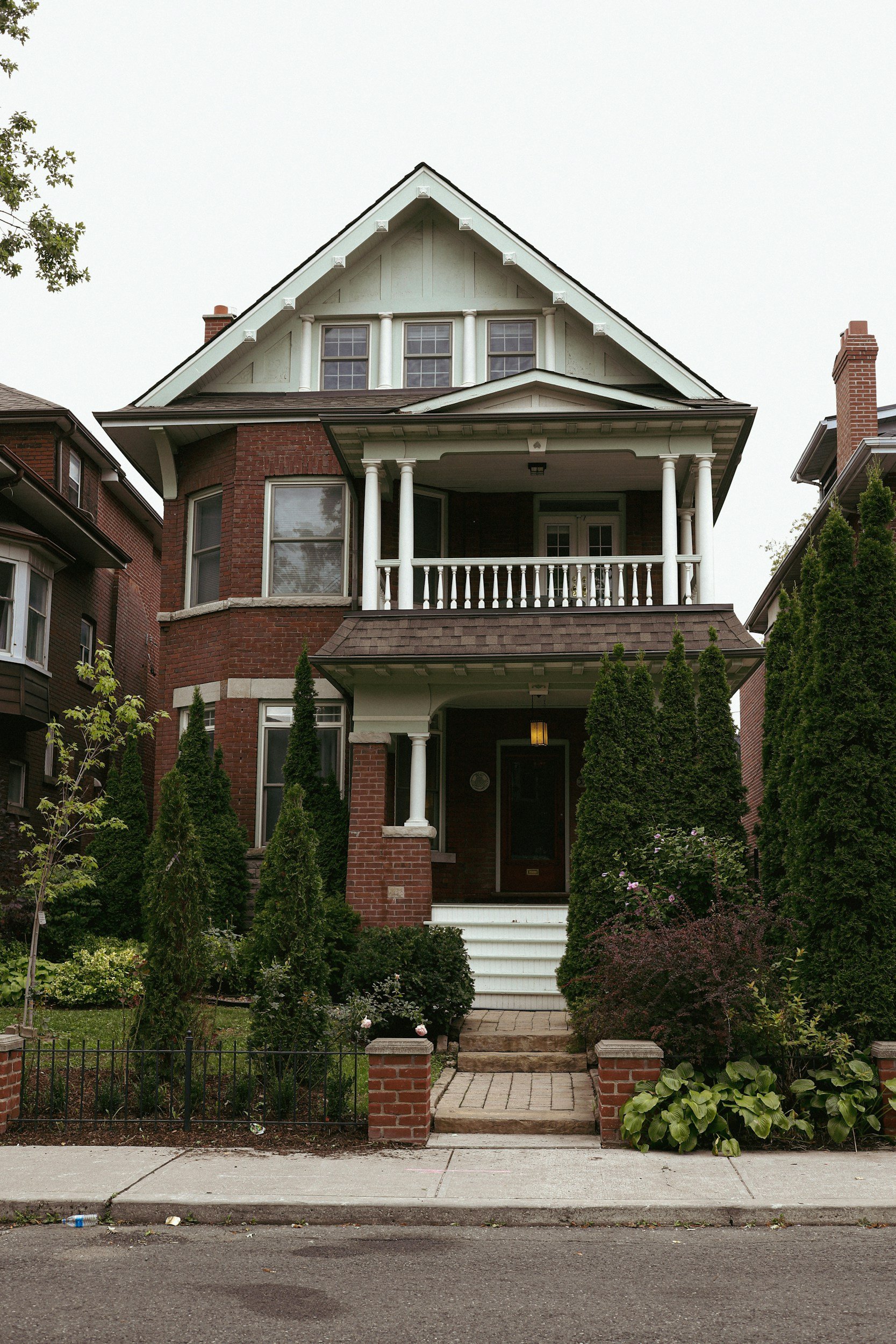 Classic brick Toronto home with a front porch, steps and a green garden