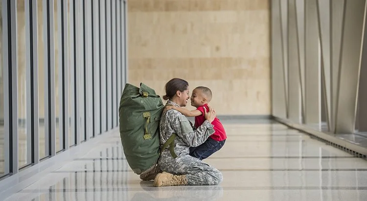 Military vet returning home, on her knees greeting a small child.