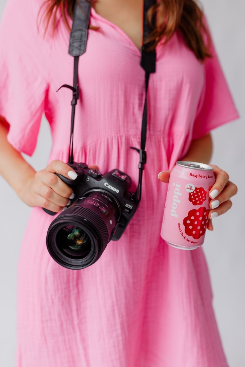 Woman in pink dress holding camera and pink drink for brand photo