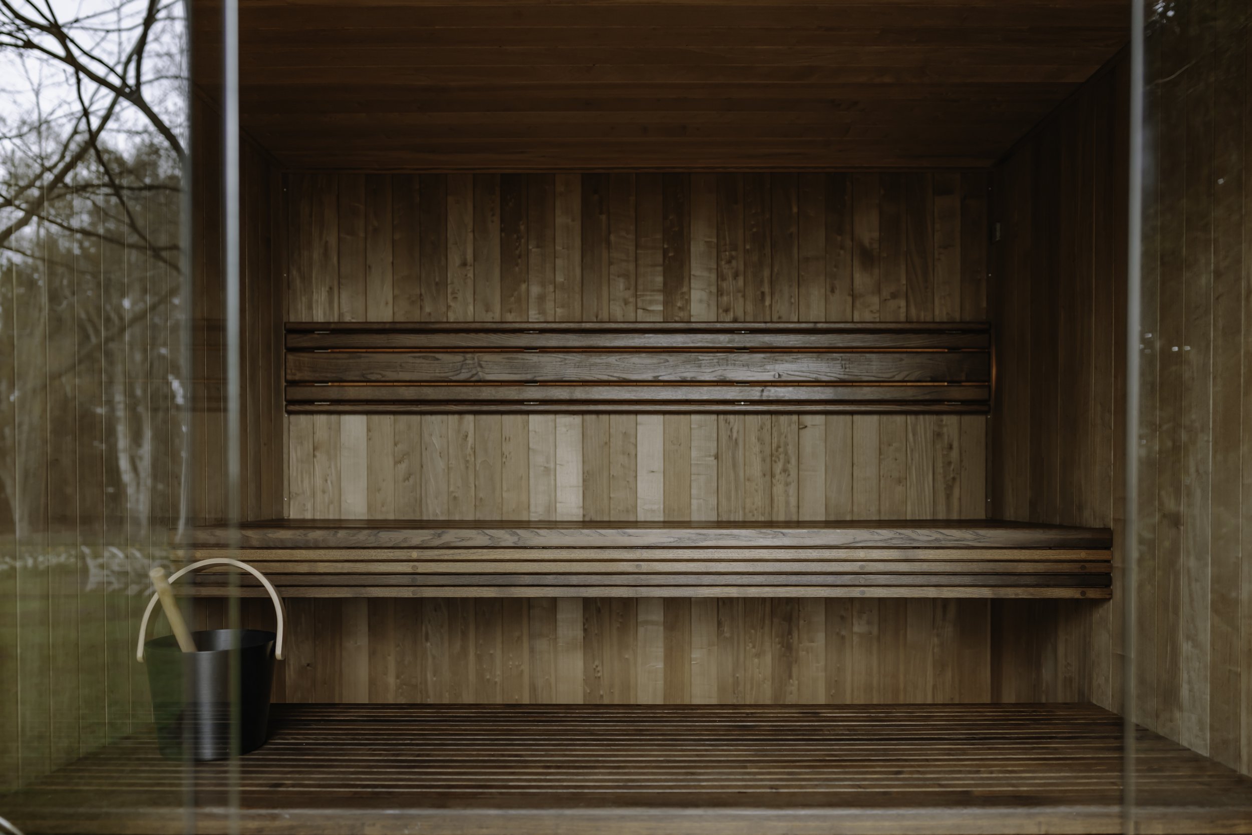 Inside view of a wooden outdoor sauna with benches and a sauna bucket with a ladle in the corner.