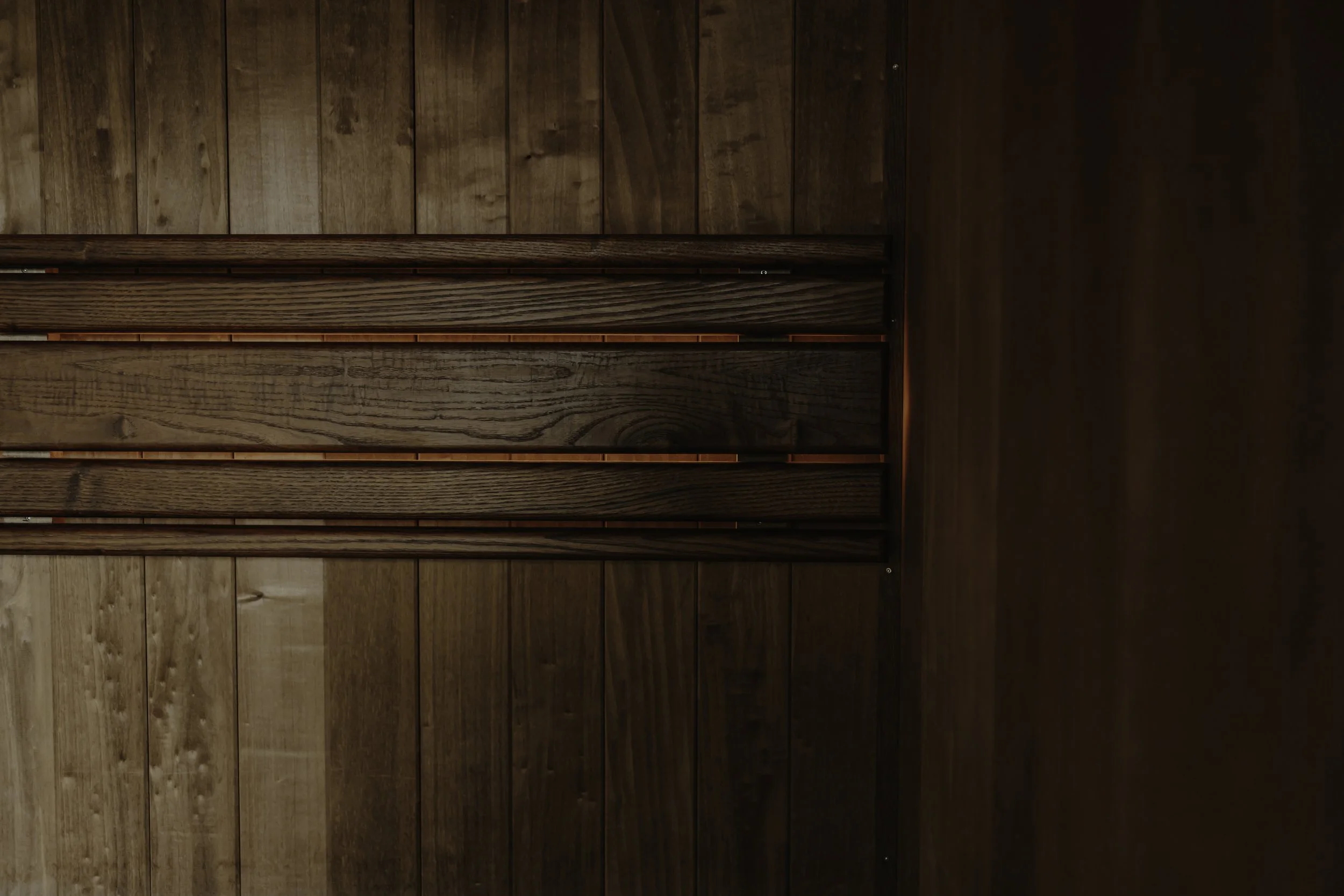 Close-up of the interior of a wooden sauna with horizontal wooden slats and small lights behind them.