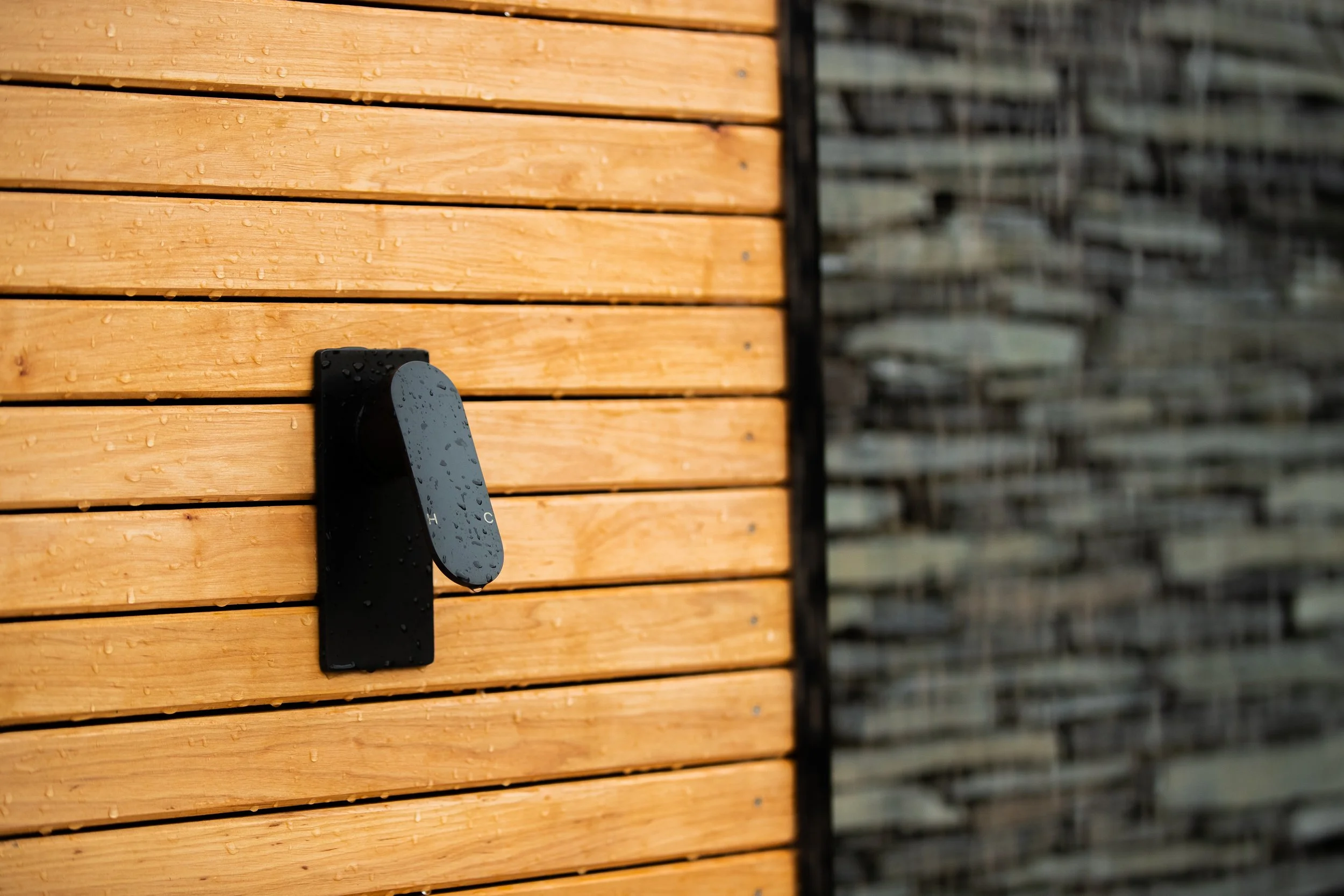 Water droplets on a black and grey outdoor thermostat mounted on a wooden wall of an outdoor shower.